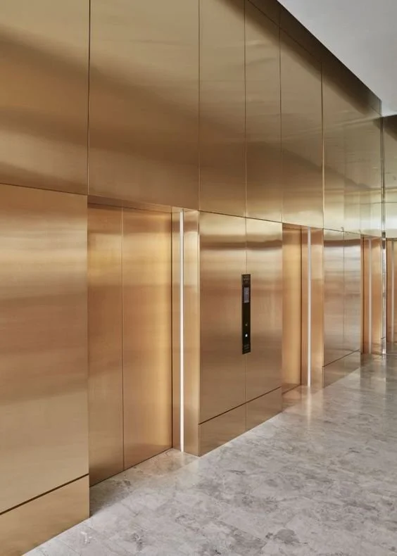 Golden elevator doors and control panel in a modern building hallway.