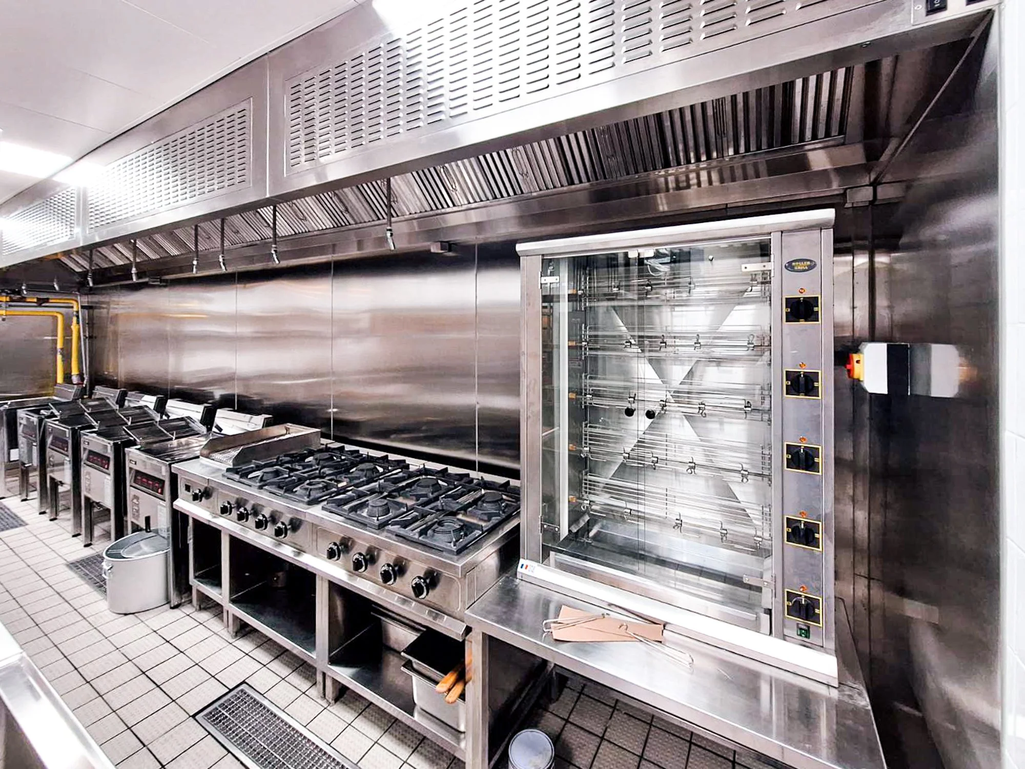 Commercial kitchen with stainless steel appliances, including a large stove with multiple burners and a drying oven, in a professional setting.
