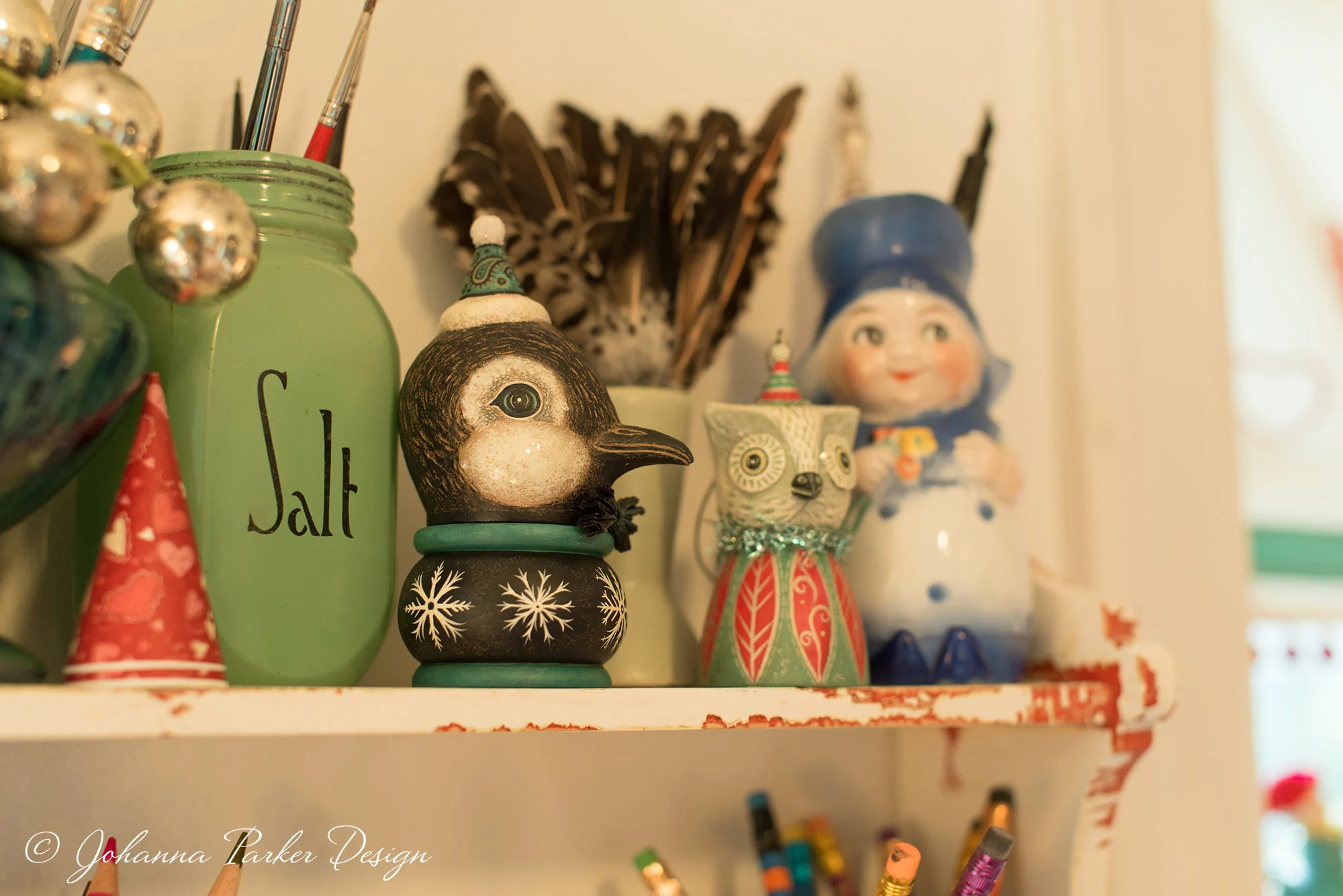 A closer peek at my shelf reveals a sweet penguin kettle cup and an owl ornament bell. Everything from feathers to vintage pottery and glassware add functionality and design inspiration to where I sit to sculpt and paint.