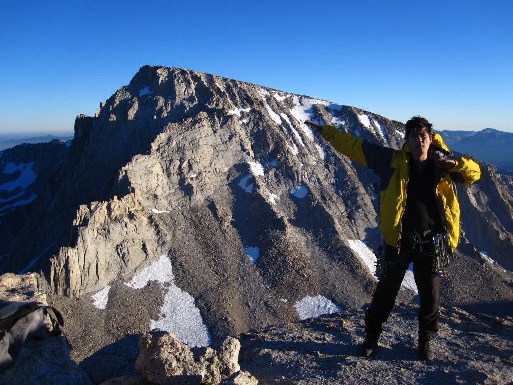 Scotty at home in his yellow jacket, on top of Mt. Russell, with a rooftop view of Mt. Whitney