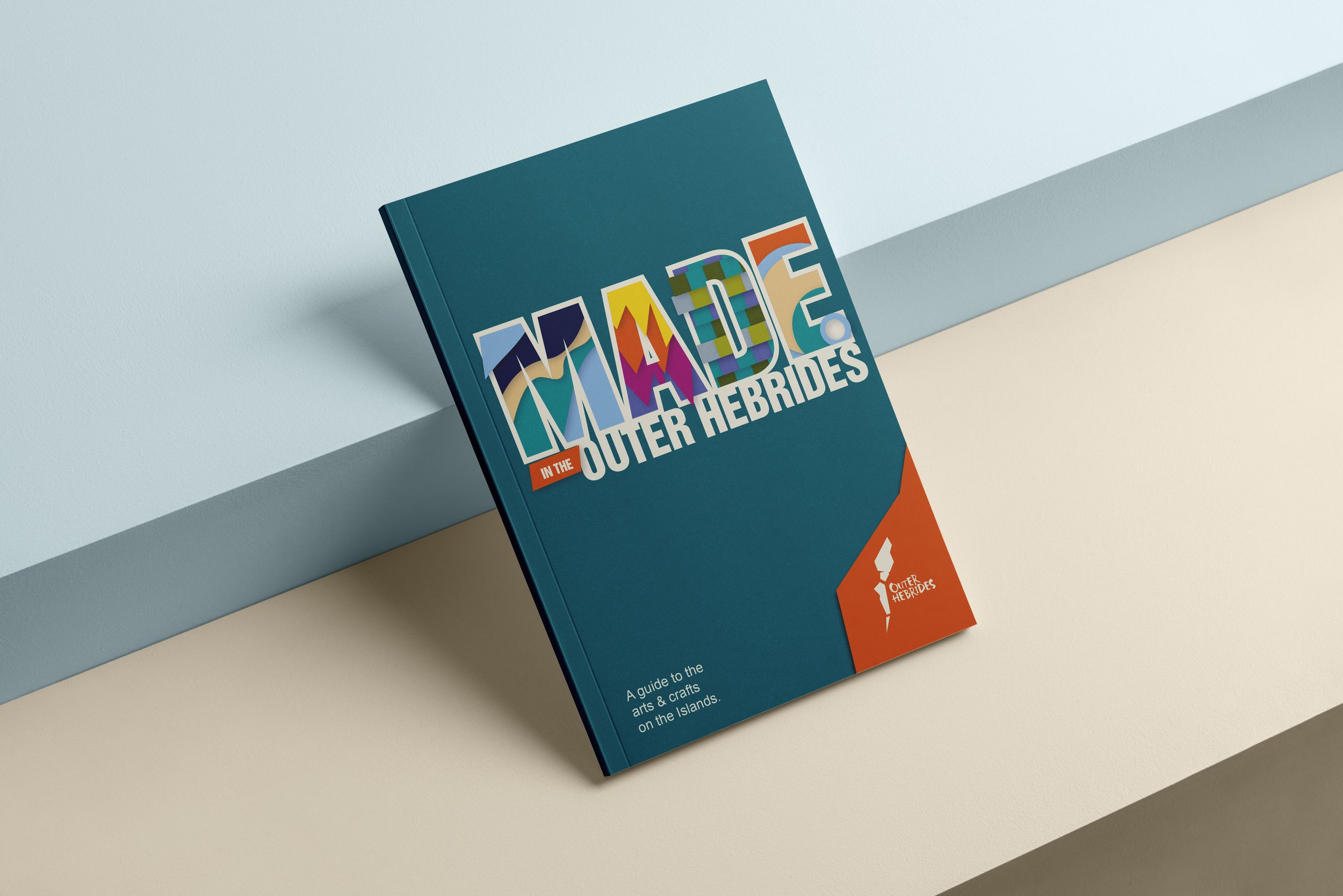 Book titled 'Made in the Outer Hebrides' with colorful text on a teal cover, placed on a white surface against a teal wall.