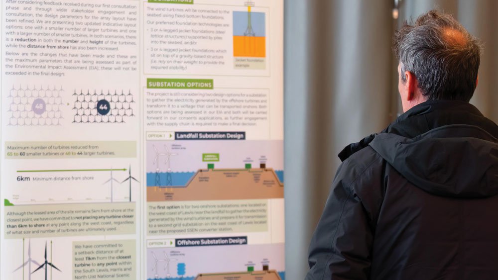 A man with gray hair in a black jacket viewing a detailed informational poster about substation options, landfall, off-shore substation design, and turbine placement.