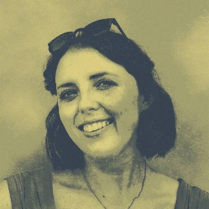 A woman with shoulder-length dark hair, glasses on head, smiling in a close-up portrait.