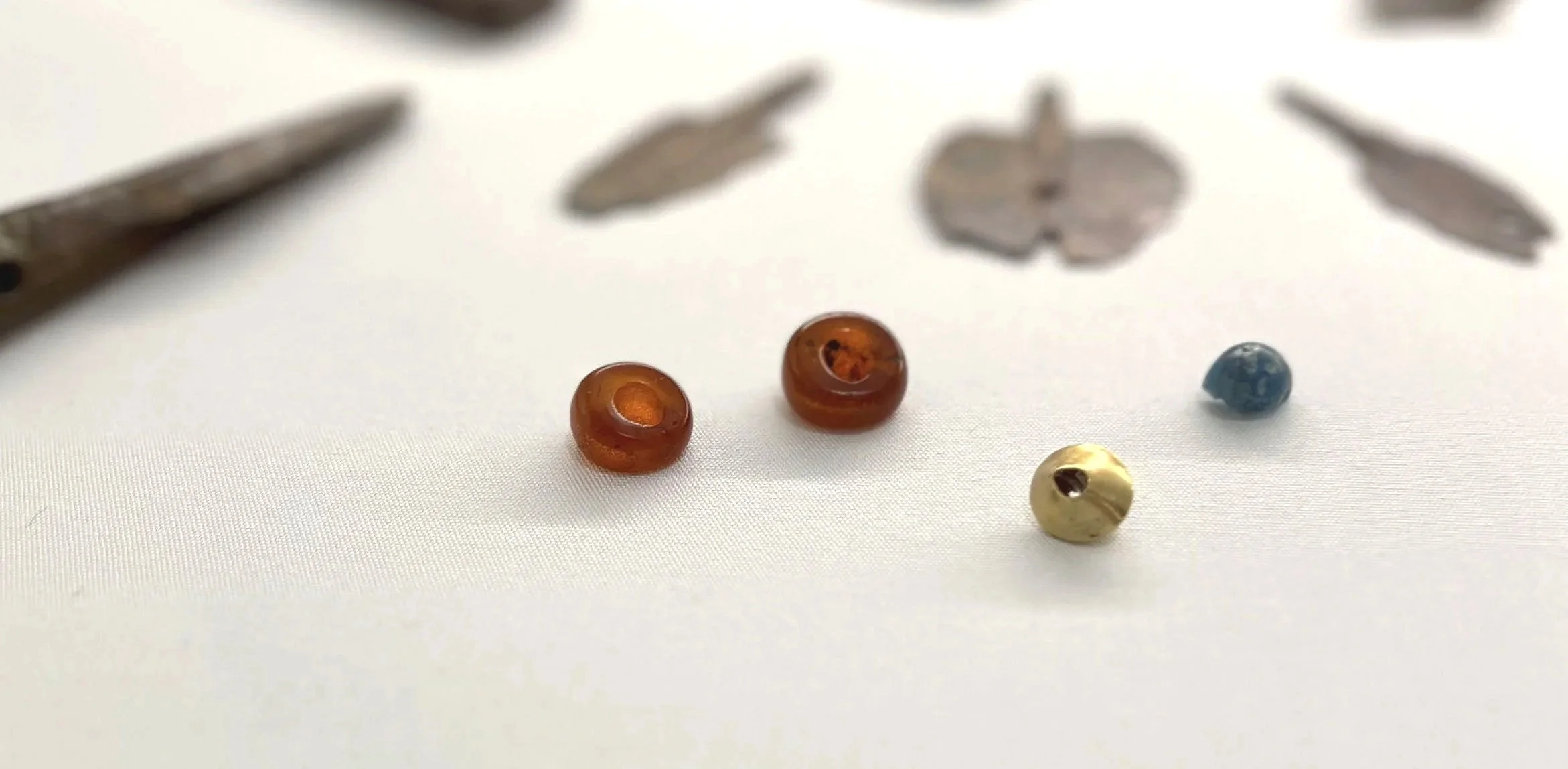 Close-up of small beads and jewelry tools on white fabric.