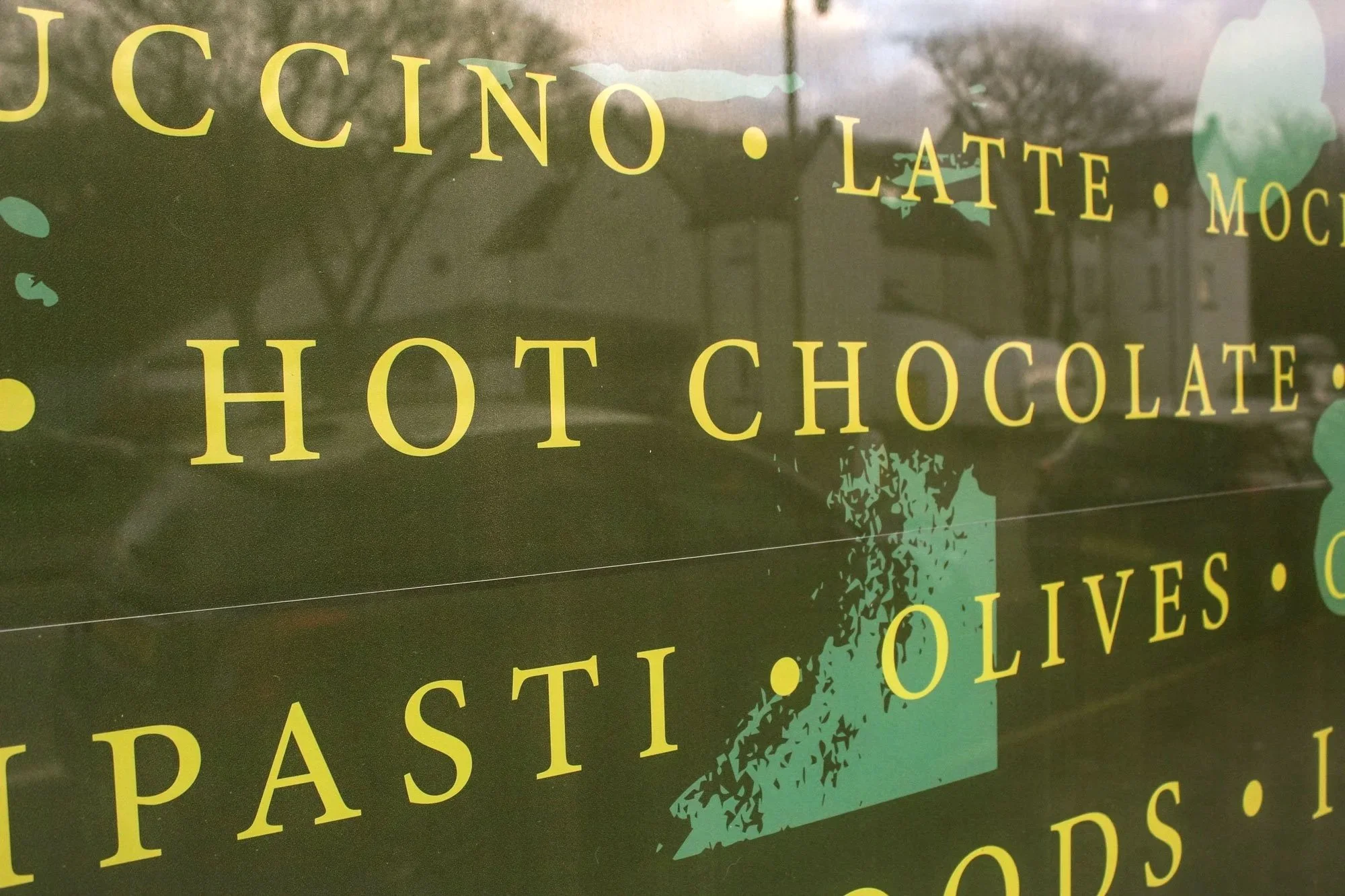 Sign with text listing coffee and chocolate drinks and snacks, including 'Hot Chocolate,' 'Latte,' 'Mochas,' 'Pastries,' 'Olives,' and 'Croissants'.