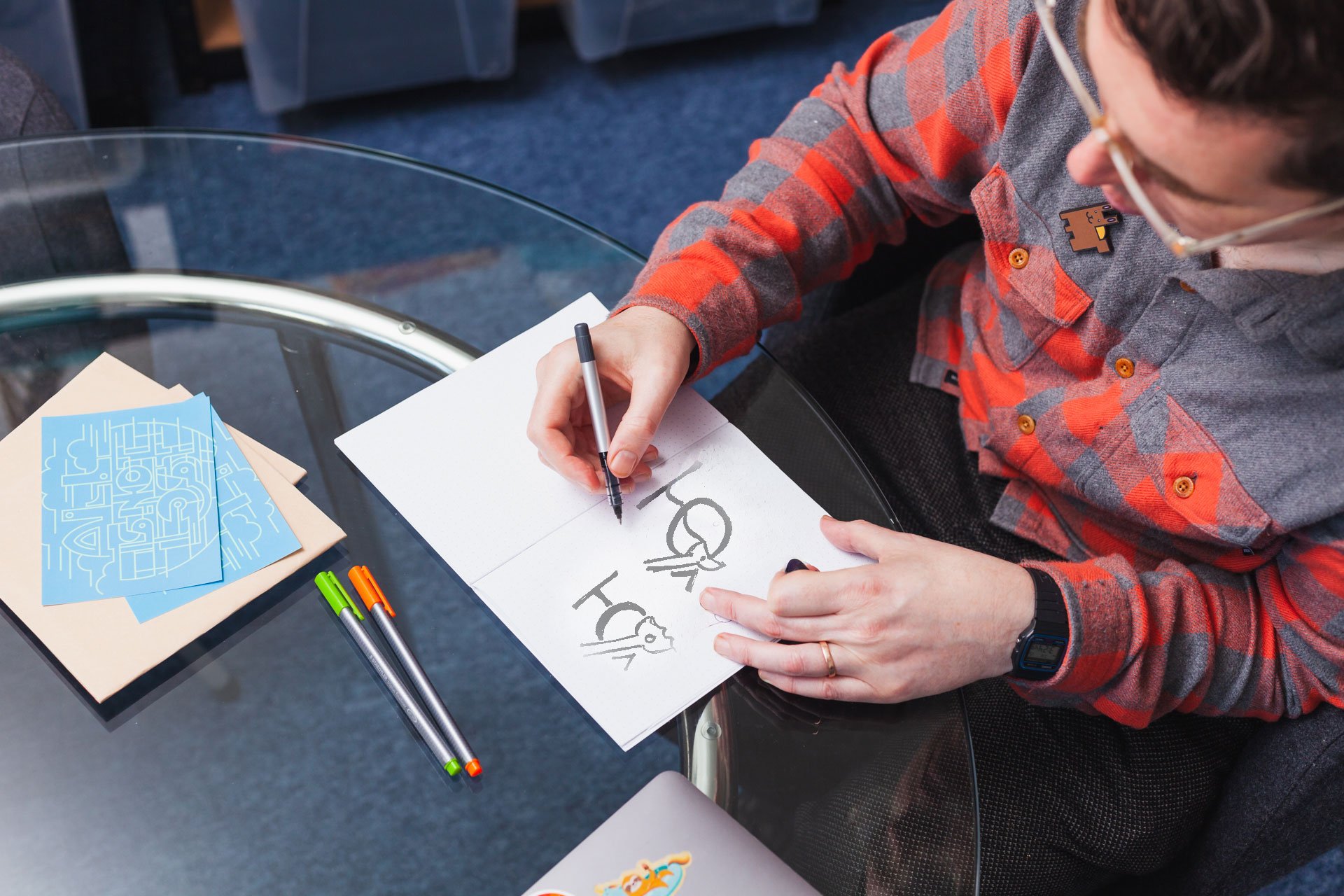 Graphic Designer Pearse O'Halloran sitting at a desk and sketching logo designs in his notebook.