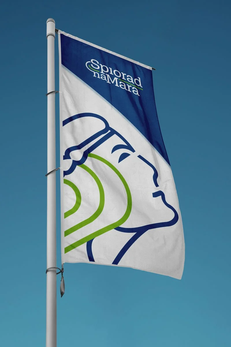 Flag with the logo and name of Sporado na Mara, showing a stylized profile of a person's face in blue and green lines, flying against a clear blue sky.