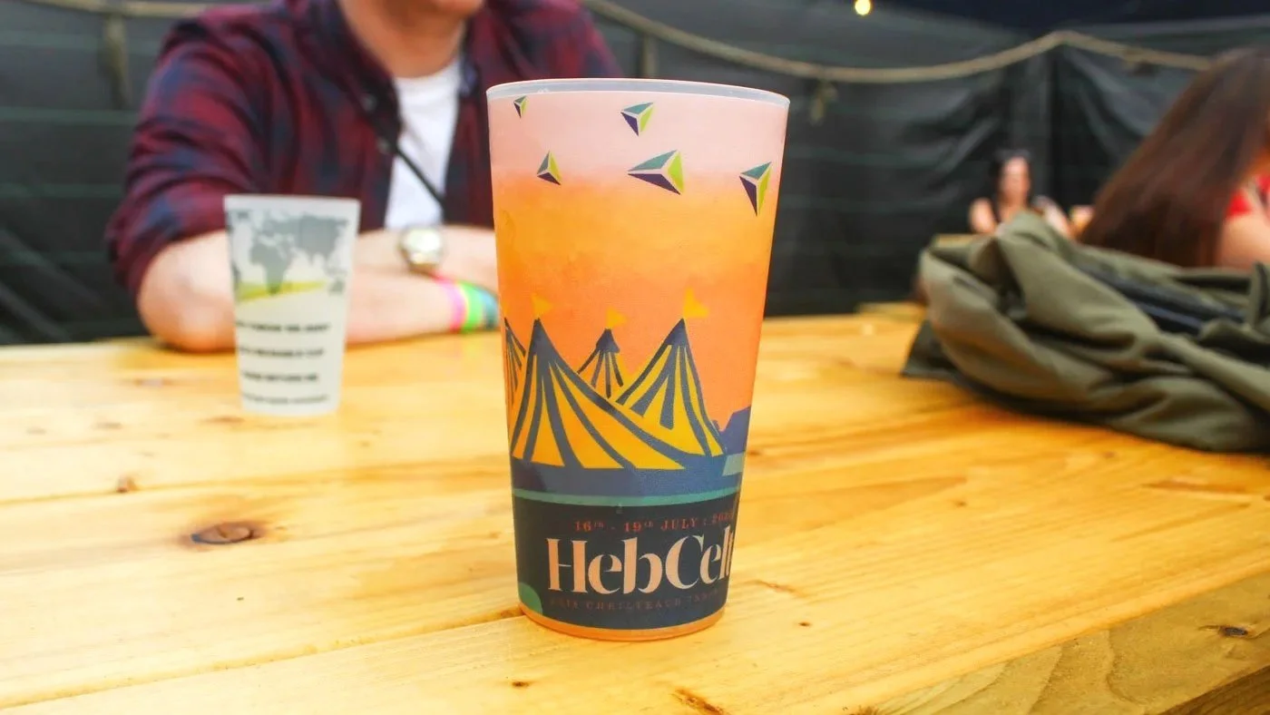 Colorful festival cup with tents and flags on it, placed on a wooden table at an outdoor event.