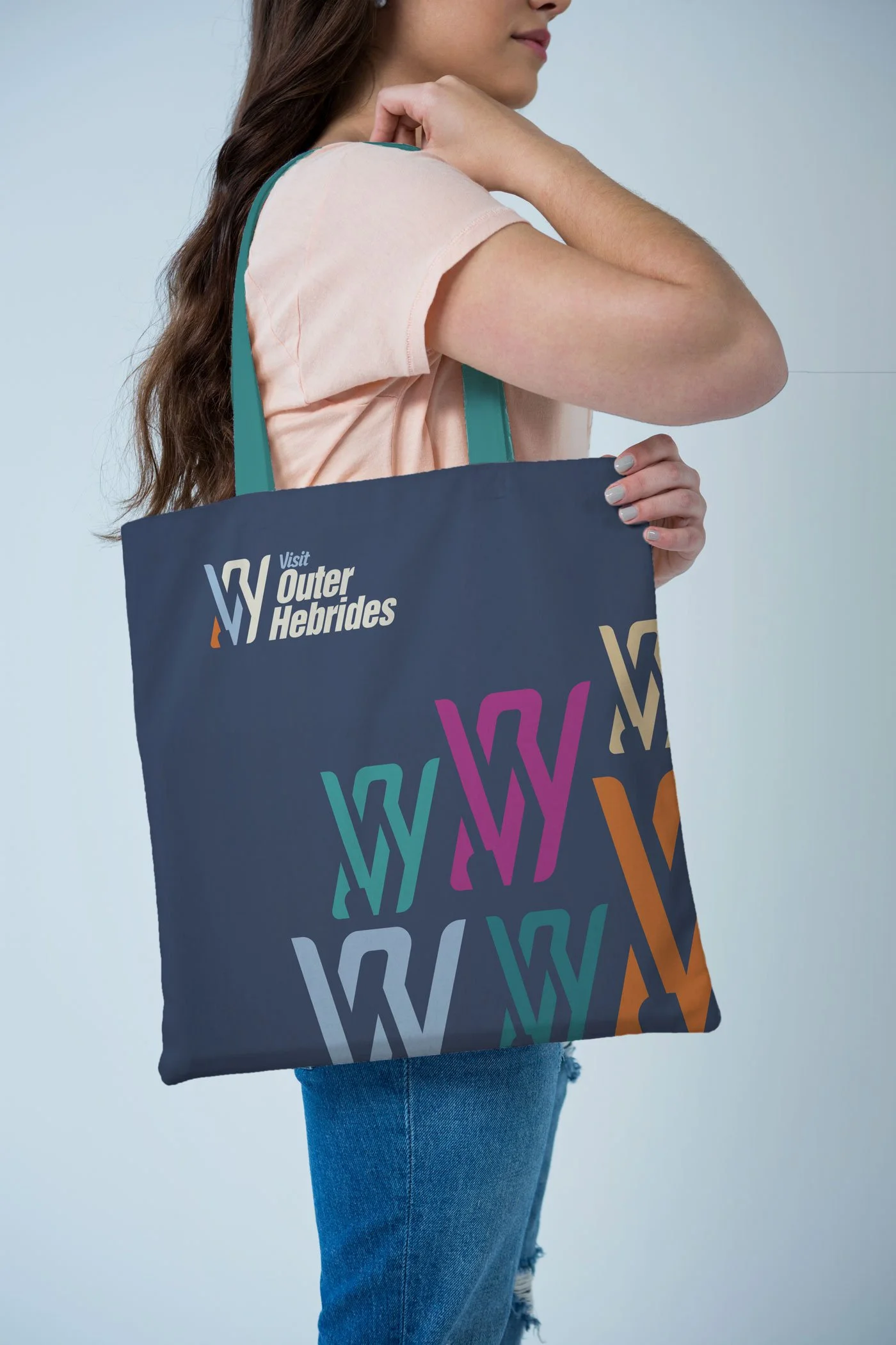 A woman holding a navy tote bag with colorful graphics and the text "Visit Outer Hebrides."
