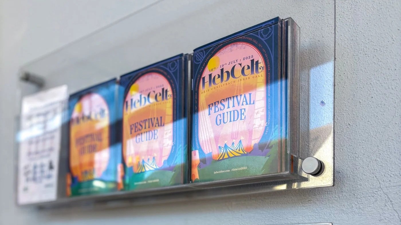 Festival guide brochures inside a transparent wall-mounted display case on a wall.
