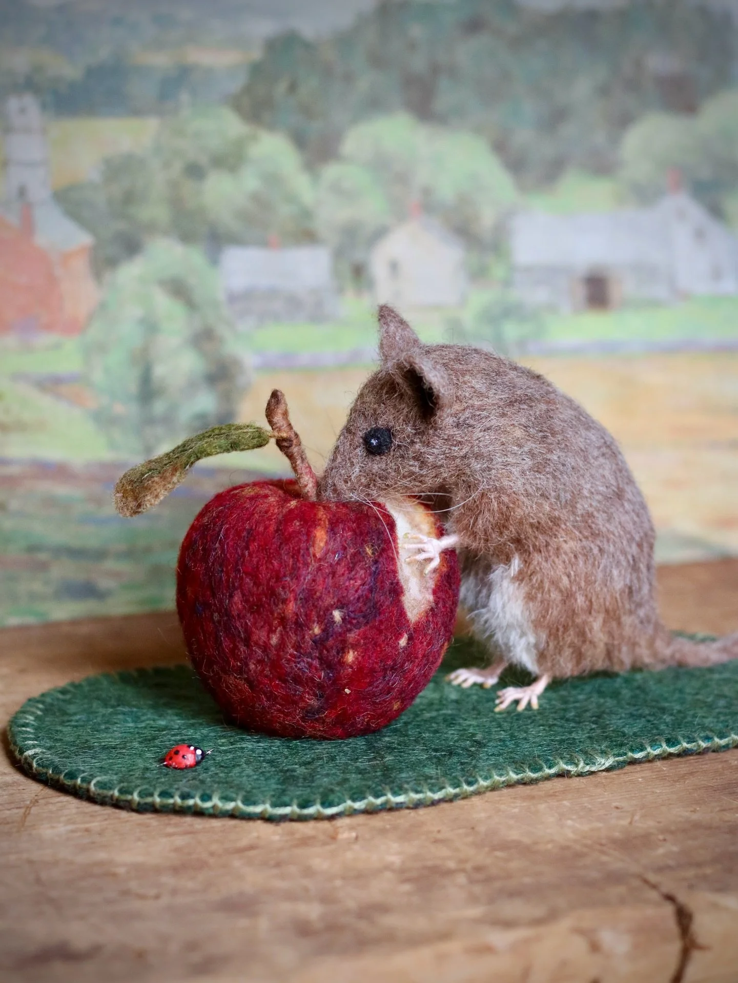 The needle felted mouse nibbles an apple as a ladybug alighted nearby observes the scene. 
The mouse and apple are needle-felted wool on a base of wetfelted wool and edged with embroidered stitches. A handmade ladybug made from wire and painted epoxy