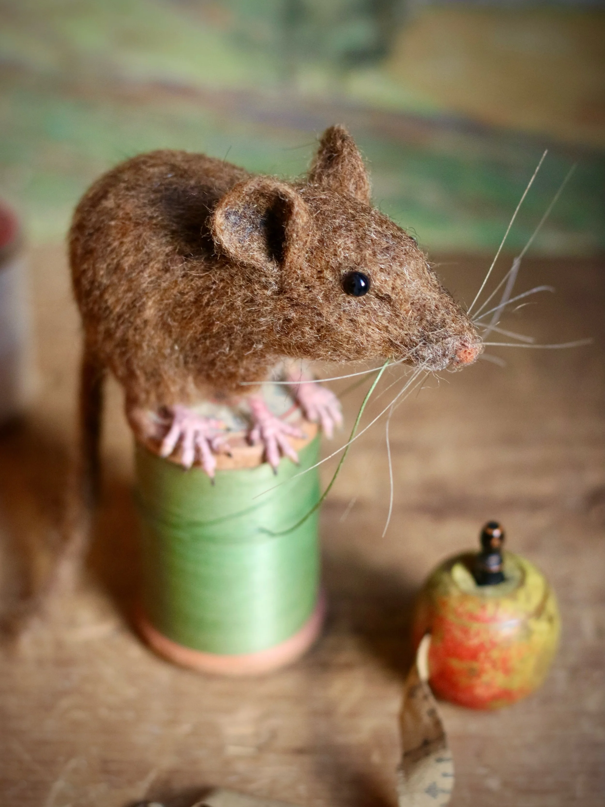 Just listed on my website! 
This life-size needle-felted wool mouse sits atop a wooden spool, playfully tugging on the thick green thread with its mouth. Both the antique glass taxidermy eyes and spool of thread were purchased at an estate sale in a 