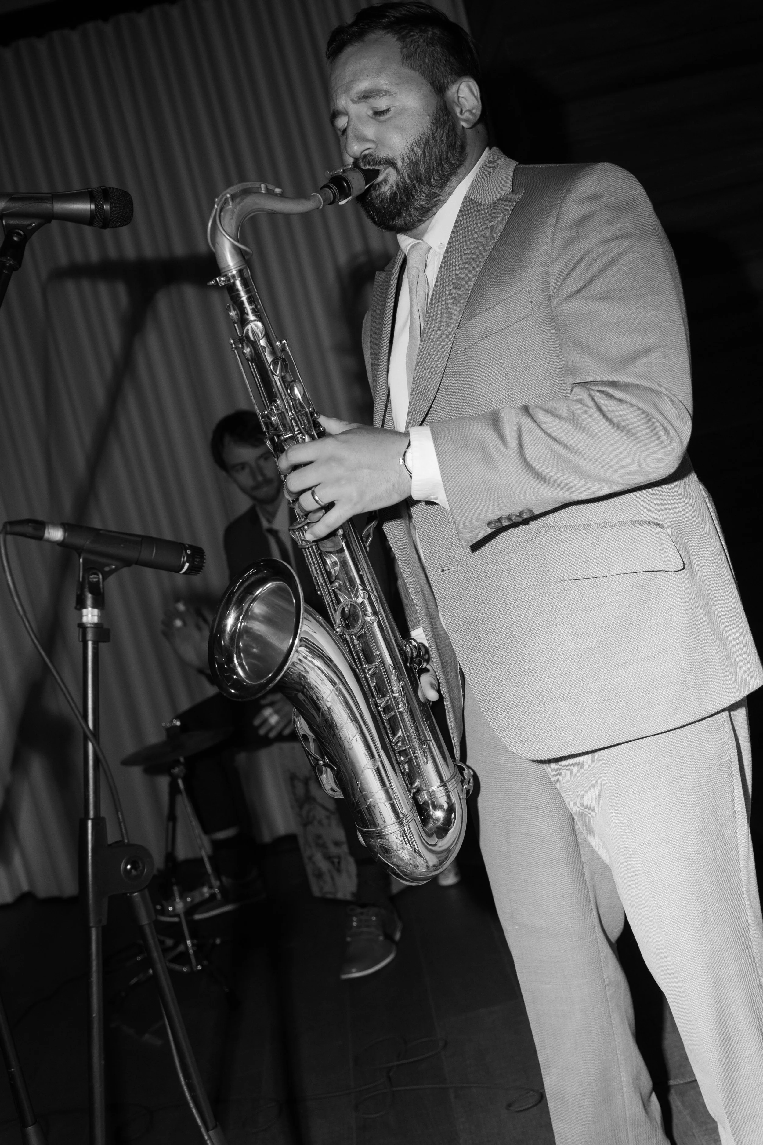 Man in a suit playing a saxophone on stage with a microphone in front of him
