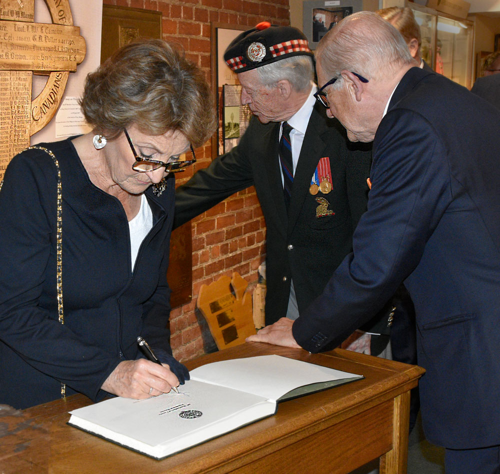 HRH Princess Margriet of the Netherlands signs the 48th Highlanders Museum visitor book as her husband learns about the Vimy Cross, currently on loan to the Vimy Ridge Canadian Visitors and Education Centre in France.