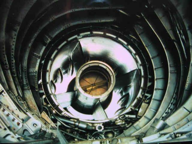 This is a photo of the center body and inlet of an A-12 looking forward from inside the nacelle with the engine removed.The center body is where the spike is mounted. The raised bumps on the perimeter are called mice and the openings in between them are the by pass door vents.The AFCS and later the DAFICS computer controlled the spike and by-pass doors to bleed off air and control air flow at the engine. (GO FAST MACHINE) Axisymmetric Supersonic Variable Geometry Inlets The conical tip in front of the engines are called the "spike". The spike moves forward and aft within the nacelle opening. Some people think, that as the spike moves aft the opening gets larger. This is not exactly true. A simplistic explanation- What happens is, the very front of the opening gets bigger but the area inside actually gets smaller. The position of the spike controls the position of the super sonic shock wave of air pressure entering the nacelle. The forward by-pass doors help stabilize and maintain the air pressure entering the front of the engine. All the extra air unneeded air is diverted around the compressor section and directly into the afterburner ejector nozzle. What this does is give higher volumes of air at altitudes where little air exist. The reason why the SR gets better fuel mileage the faster it goes, is because at those altitudes the air is so thin that there is less drag on the aircraft and the inlets create air pressures at better than sea level. The technical and engineering aspects of these inlet are vast and most people can't understand exactly how they work. I myself have spent many many hours with my body wedged up inside SR-71 inlets measuring, mapping dimensions, removing, rebuilding, and installing inlet assemblies. I can tell you this, unless I had a need to know, I didn't ask. Did Skunk Works develop the "Perpetual Motion Machine"? Even thought by this theory one might think this is the ultimate perpetual motion machine, it is not. The SR's speed is limited not by power but by temperature. As speed increases so does the temperature and when these alloys heat up bad things start to happen. They start to expand, warp, and buckle. their characteristics start to change and weaken. The SR crews were not to let inlet temperatures exceed 427 degrees C.