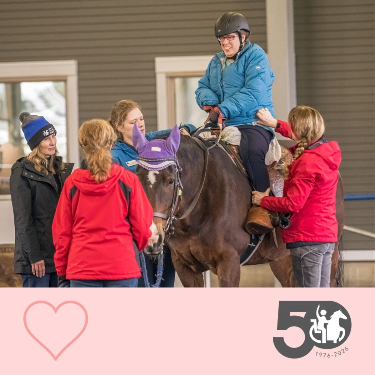 Participant sits confidently on a horse while volunteers and staff stand nearby providing support.