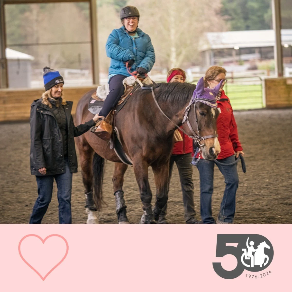 Participant rides a horse through the arena with volunteers assisting on both sides.