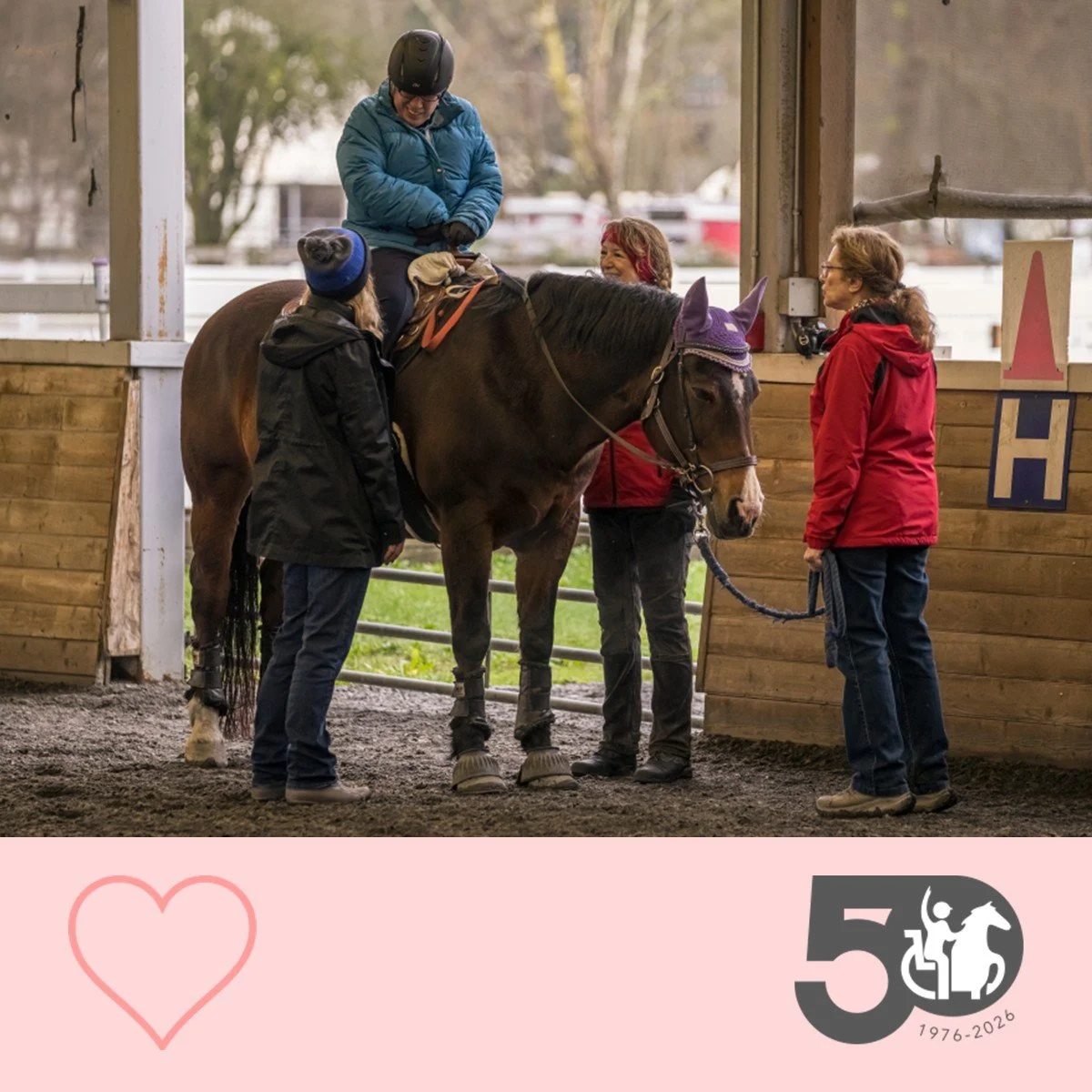 Participant sits on a horse while volunteers pause together during an adaptive riding session.