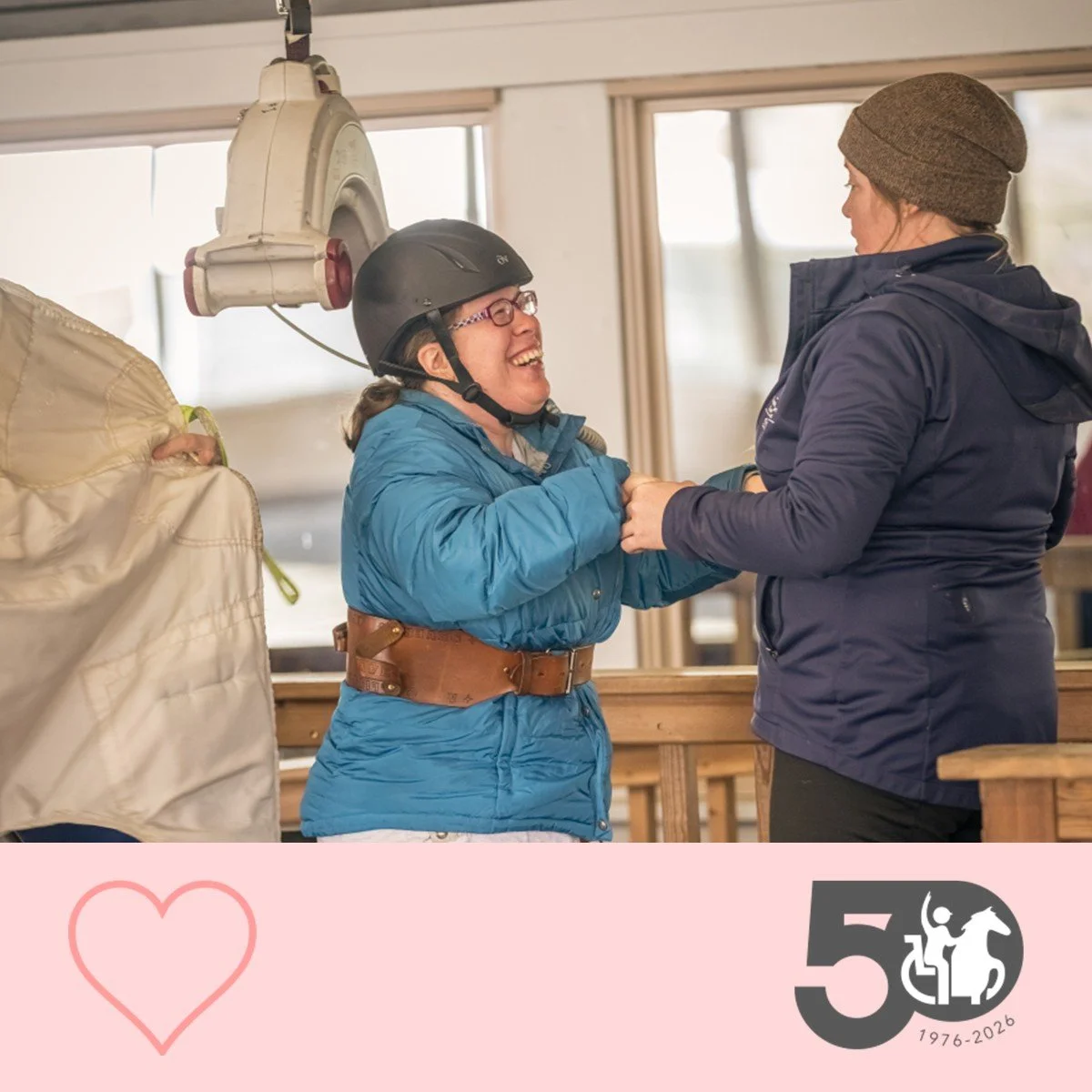 Participant smiles while being supported by staff. A hoist lift is noticable in the background.