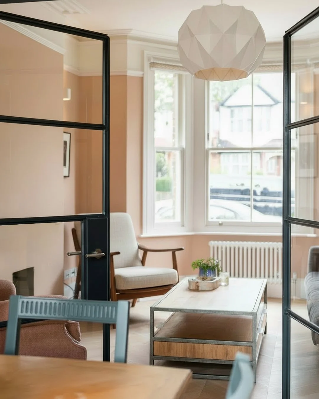 The front living room at Lordship Lane, seen through black steel-framed glazed doors, with its bay window and radiator.