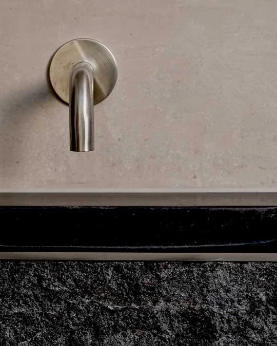 Detail of a wall-mounted bathroom tap against a stone splashback in the Lordship Lane refurbishment.