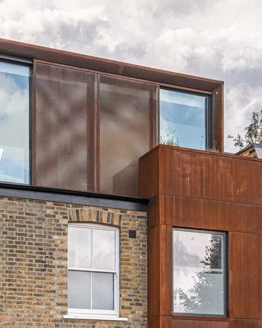 The Corten-clad loft and first-floor extension meeting the original brick façade at Lordship Lane, with a sliding perforated privacy screen.