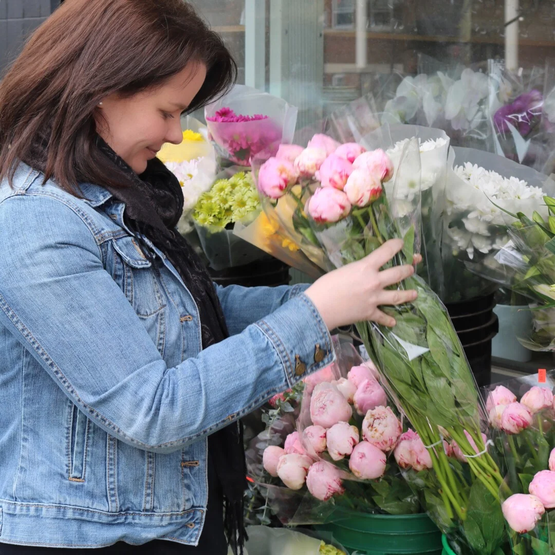 A woman in a denim jacket shopping for pink and white peonies at a flower shop.