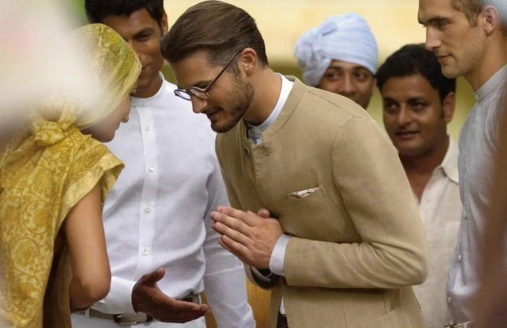 A Western man and an Indian woman engage in a respectful greeting, surrounded by other Indian men, during a cultural exchange or diplomatic event.
