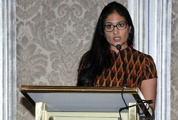 Woman speaking at a podium during a presentation or speech.