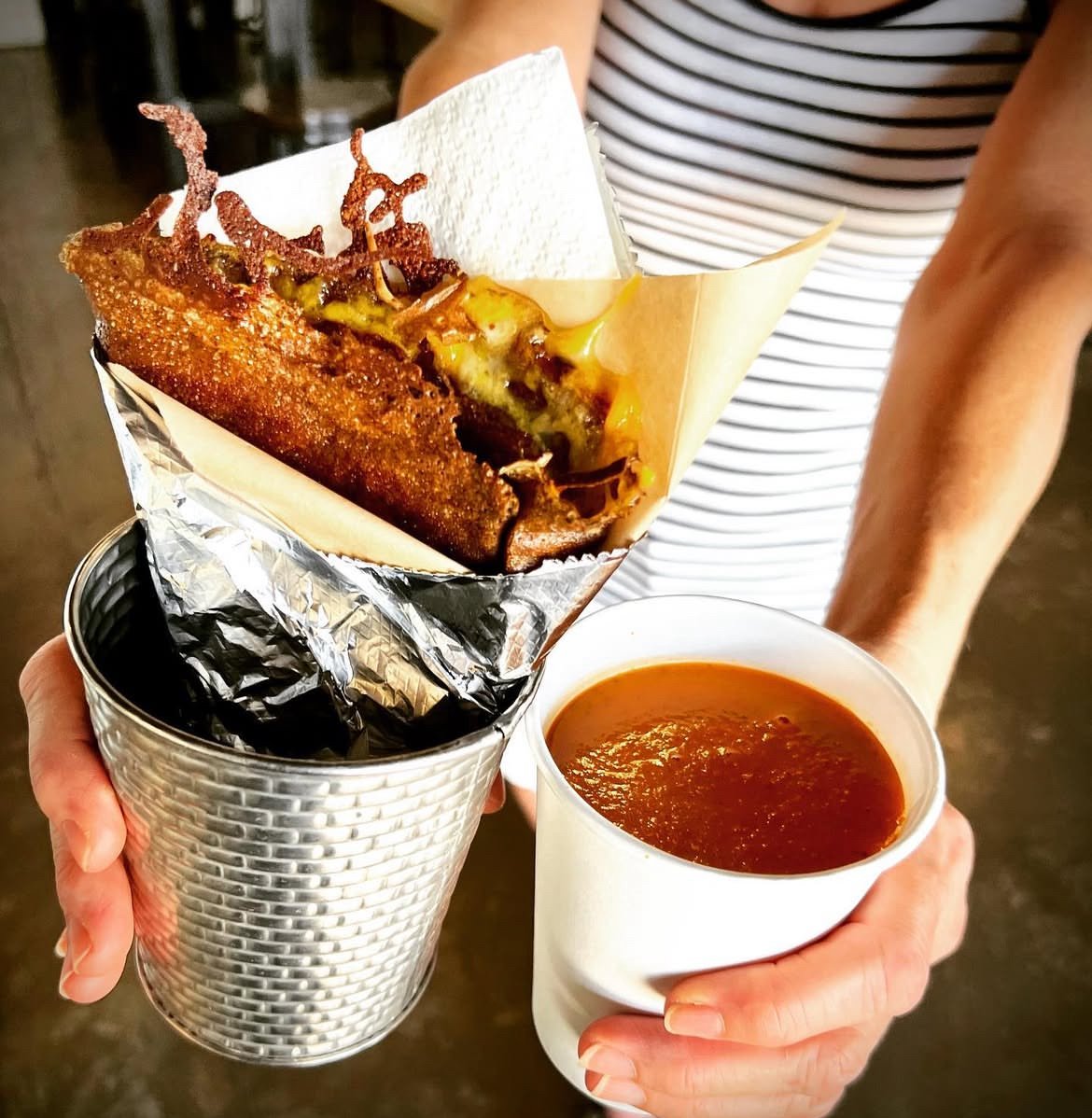 A photo showing a person holding a handheld crêpe and a cup of Sippable Soup