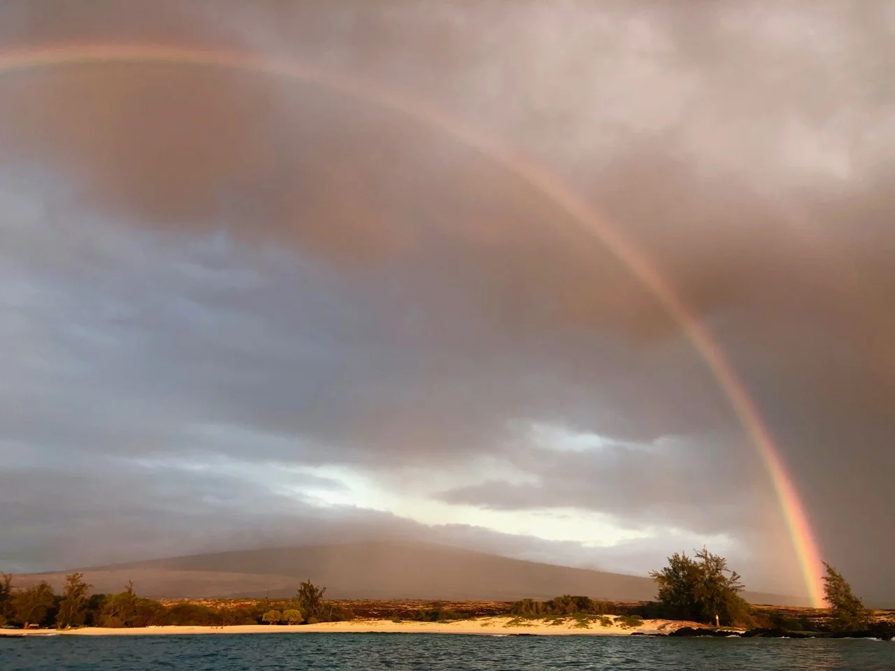 Being part of earth’s natural beauty is one of the great rewards sailors get from the sailing lifestyle. This was our view at sunset recently anchored off Makalawena Beach on Hawaii island; as the sun set behind us, the rain coming down from Hualalai volcano refracted perfectly on the beach—it’s raining shoreward but not where I took this photo. The natural world just hovered in stasis like this for 15 minutes. After staring at the scene in awe for a moment, I finally broke free and grabbed my camera to nail this shot—how often does that happen? PHOTO and CAPTION by: Paul Exner