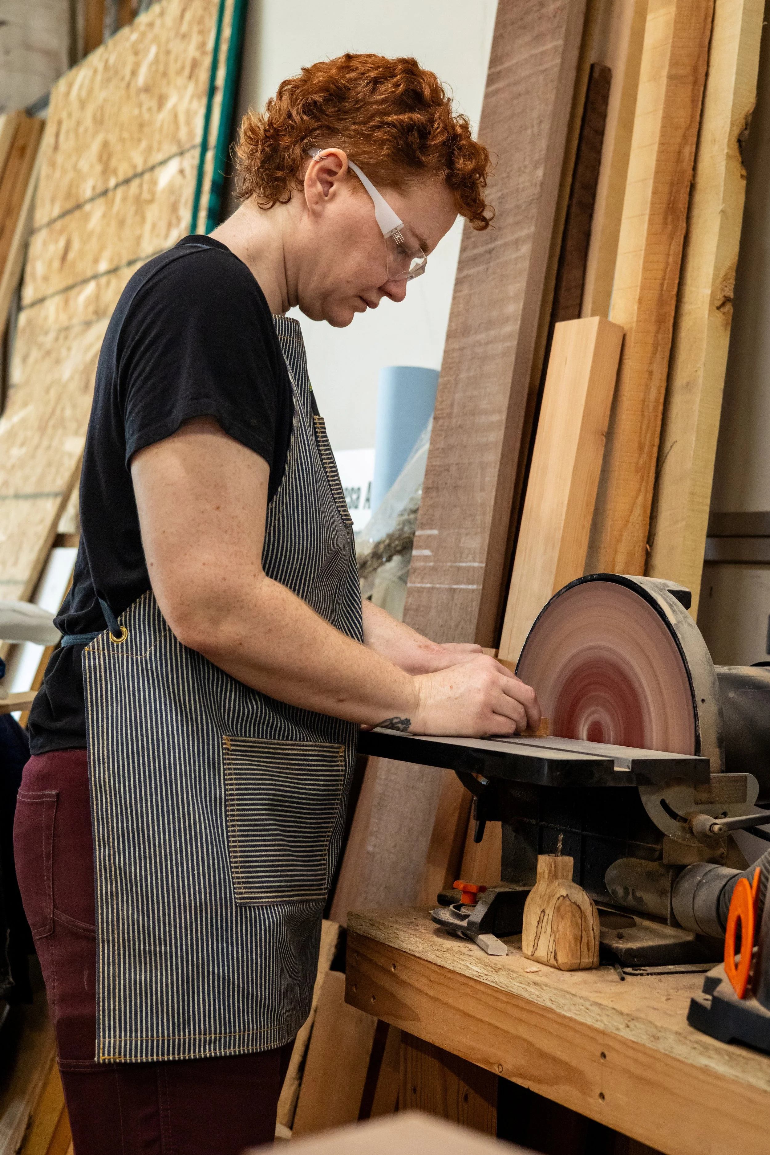 A woman in her woodshop working at the disc sander
