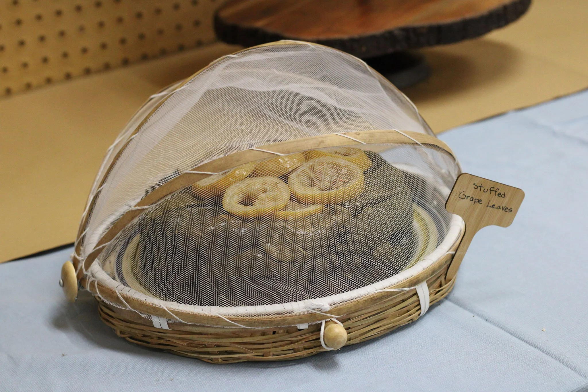 Stuffed grape leaves garnished with lemon slices and covered with a mesh food tent on a garden party buffet table.