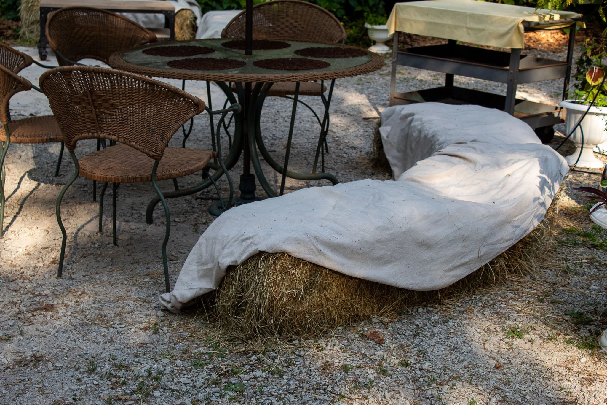 Three hay bales covered with canvas beside a wicker patio table and chairs at an outdoor garden party.