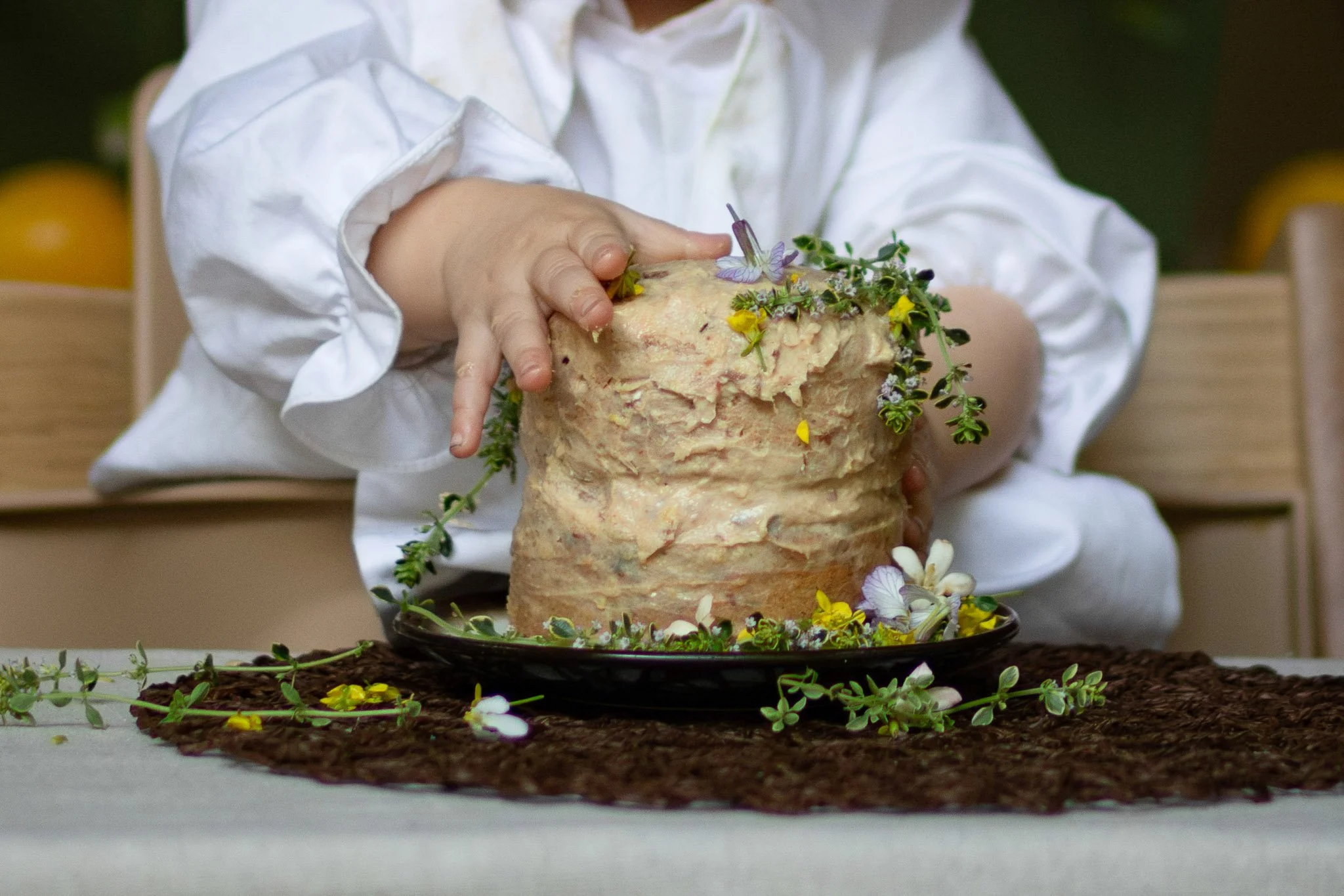 Baby touching a homemade first birthday smash cake decorated with edible flowers and herbs at a lemon garden party.