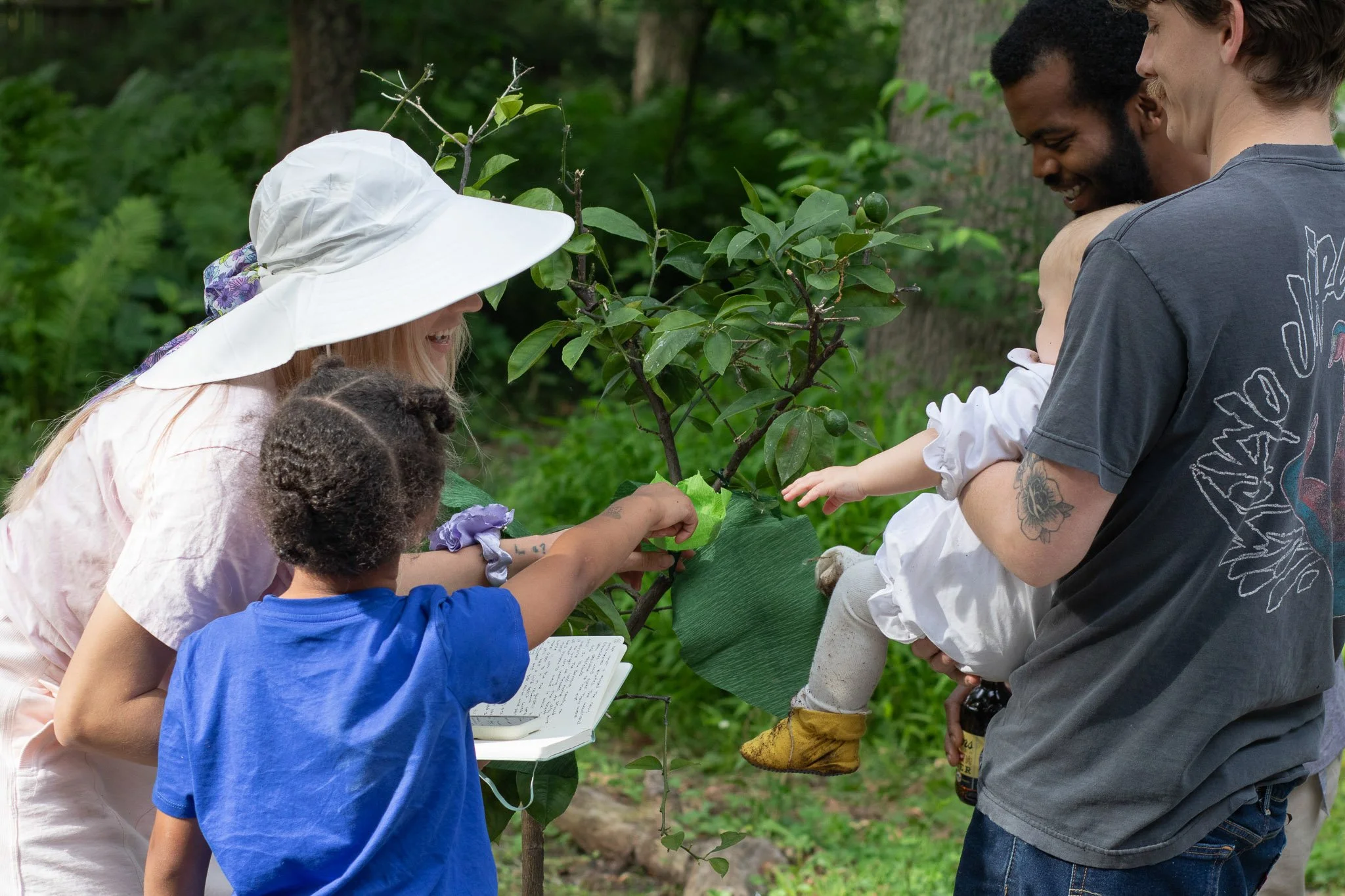 Children and adults participating in an interactive garden storytime as the birthday baby reaches toward a handmade sensory garden scene.