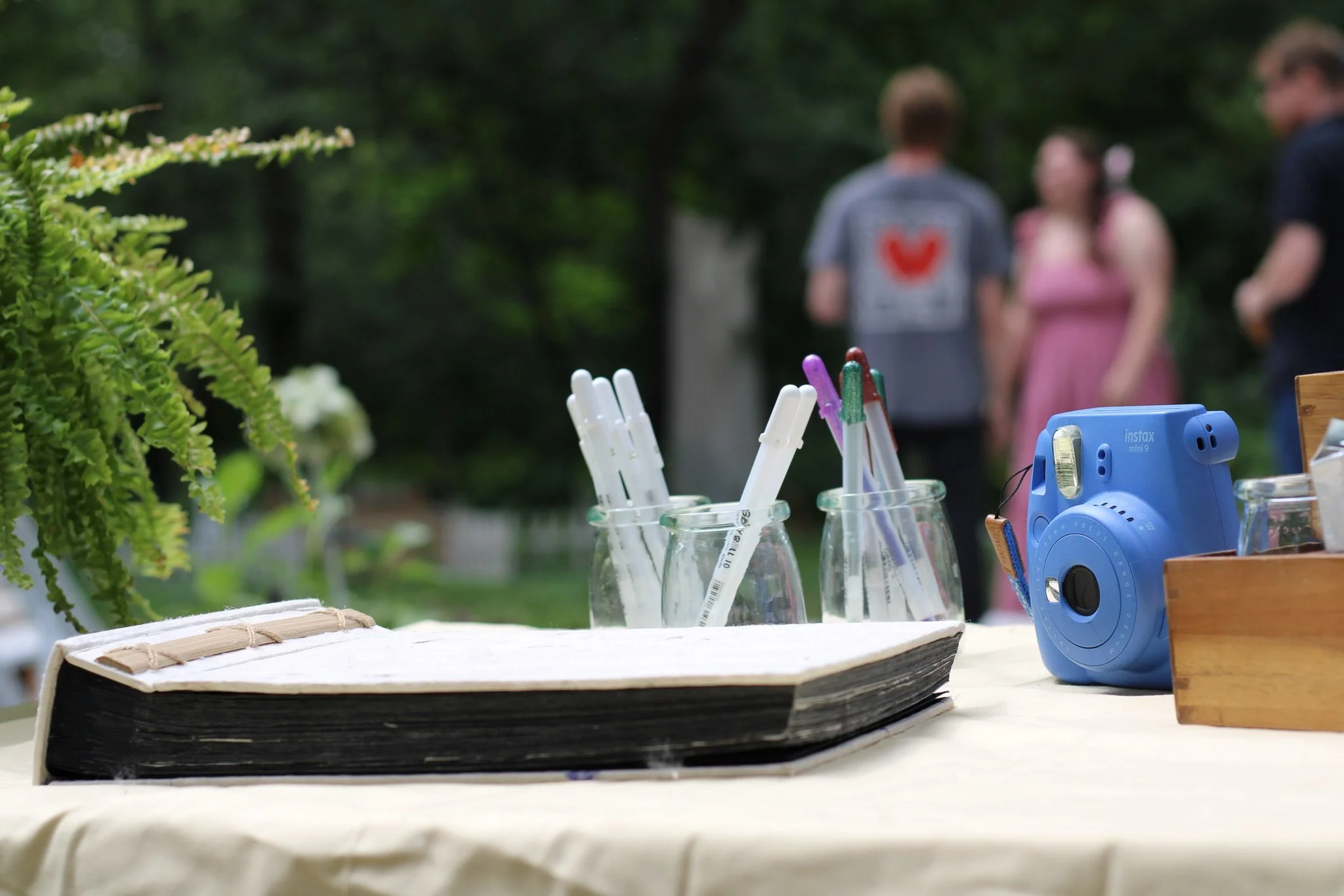 Memory book station with a blank scrapbook, pens, and instant camera set out for guests at a garden first birthday party.
