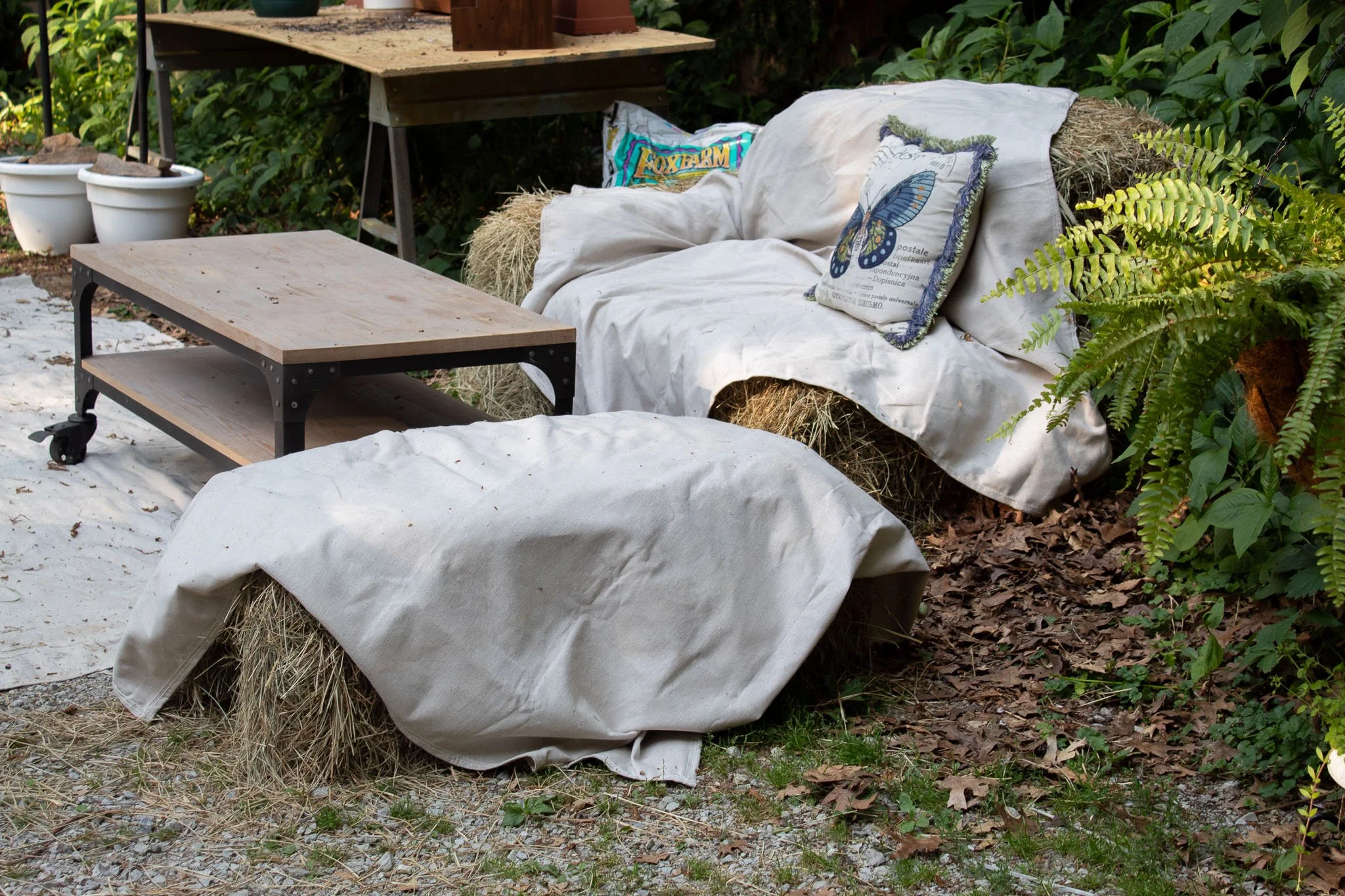 Hay bales arranged as a garden-party sofa, covered with canvas drop cloths and paired with a low wooden table.