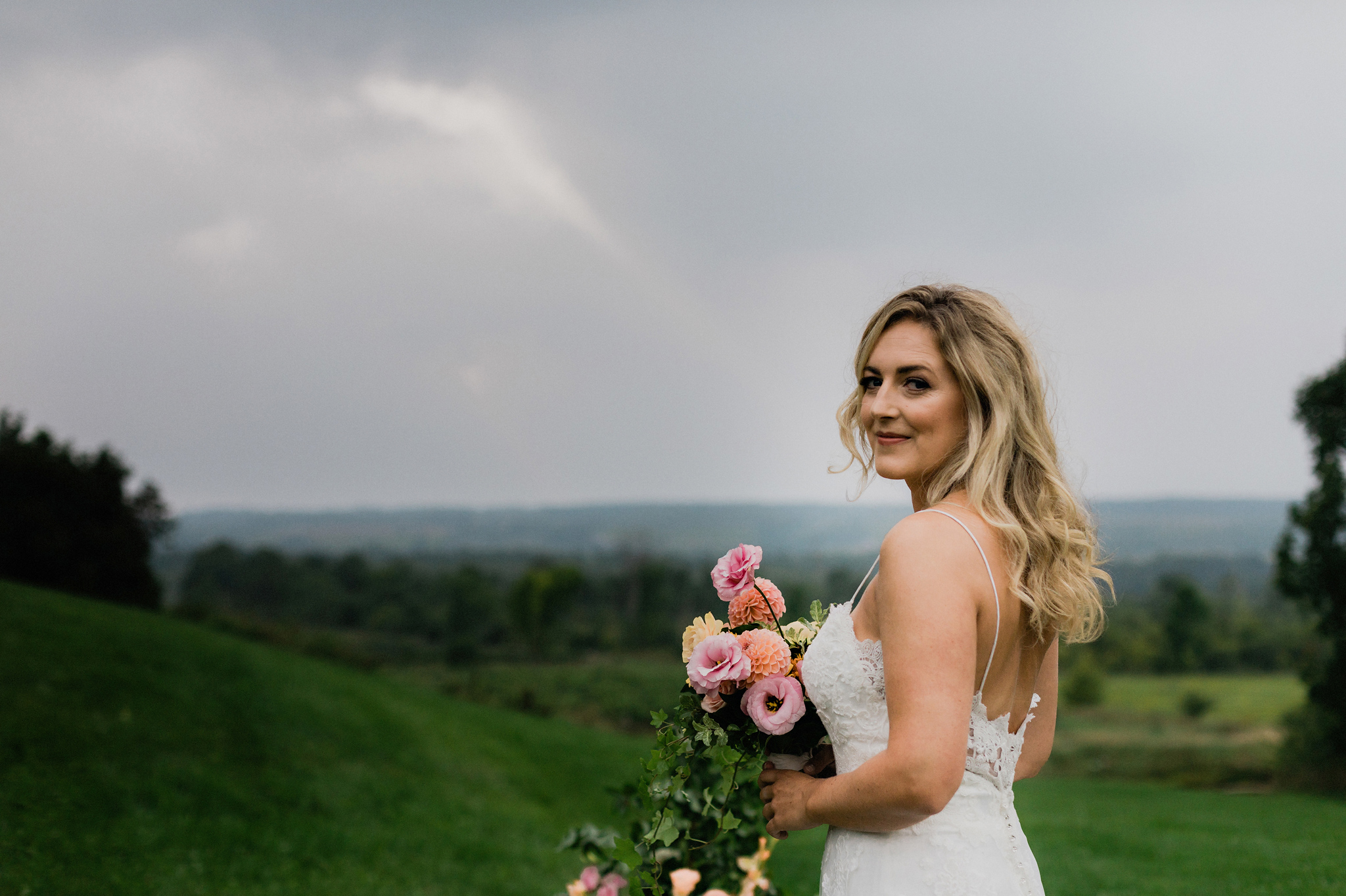 Bride with lace gown, windswept hair and a natural coral bouquet