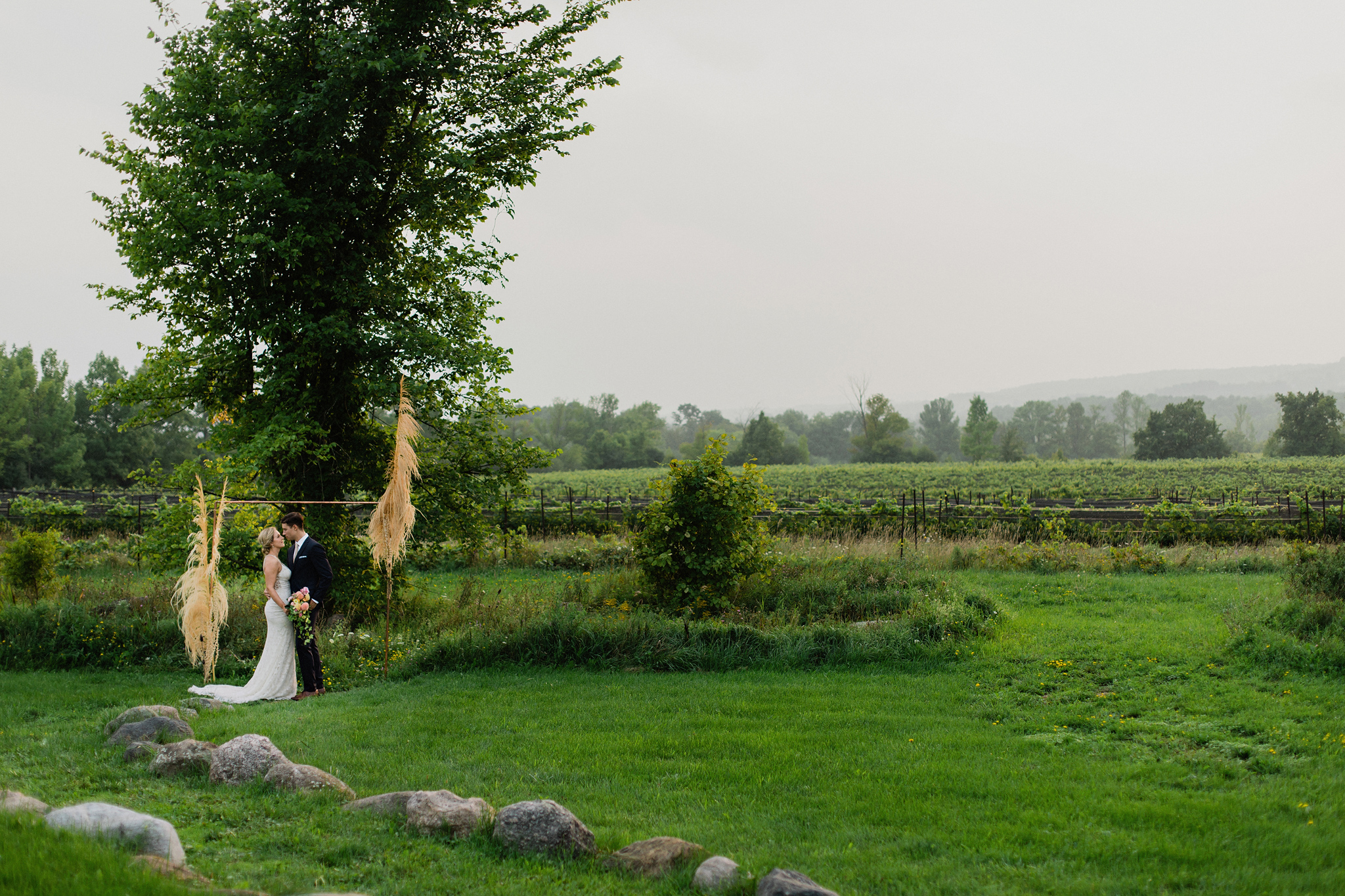 Couple stand at copper and dried grass wedding arch at Coffin Ri