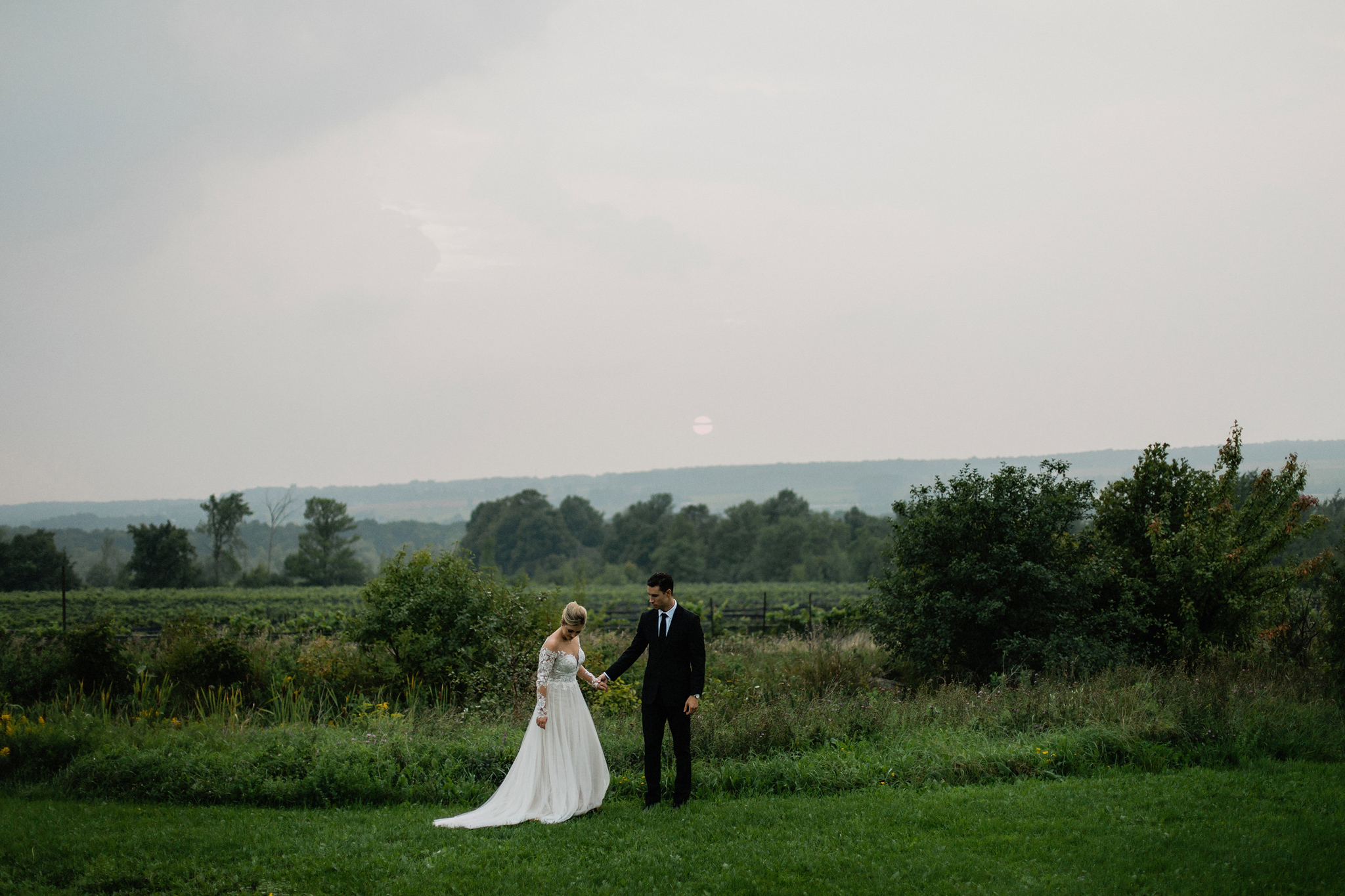Bride and groom stand in field overlooking vineyards at Coffin R