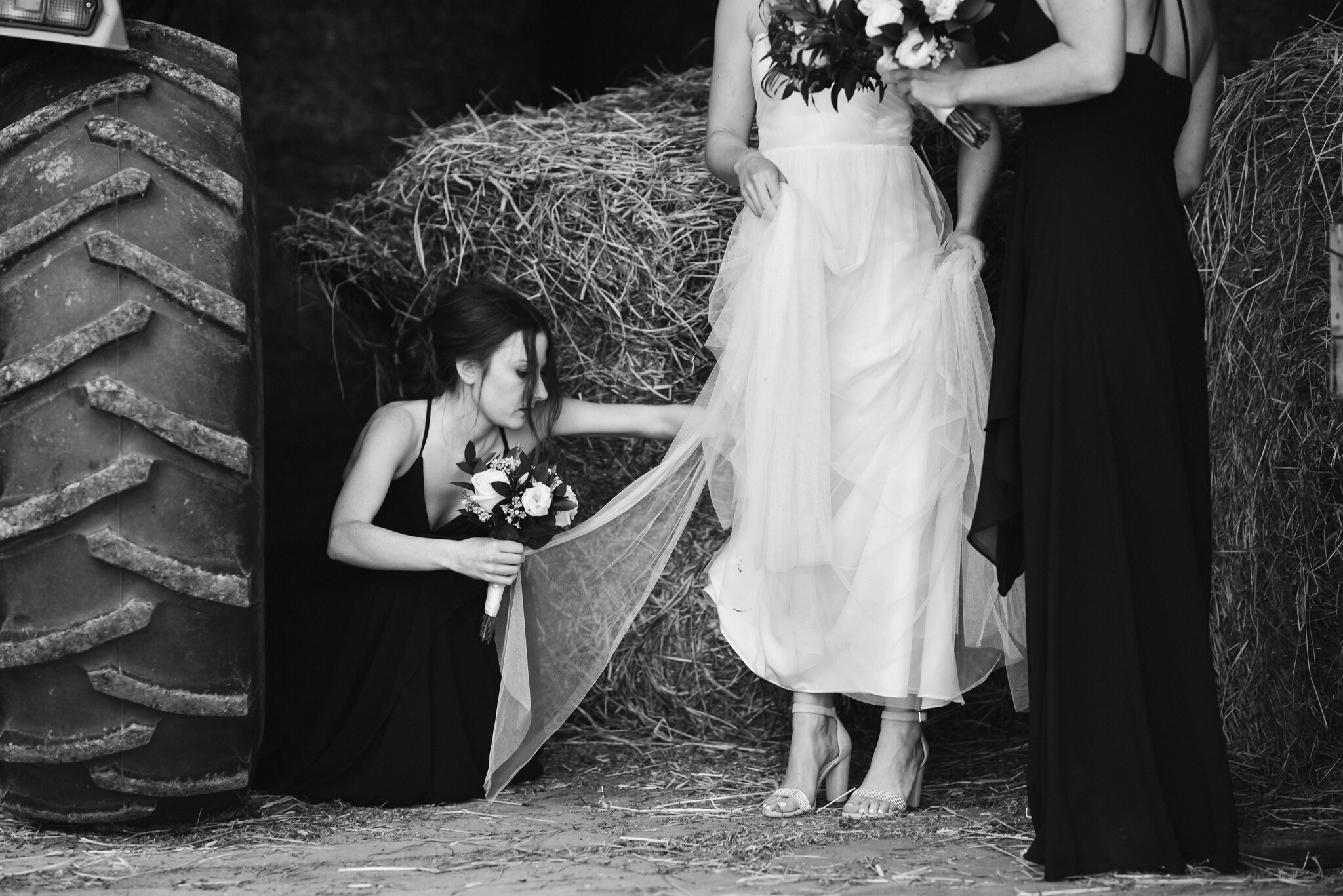 Bridal party helps with brides dress in barn before wedding