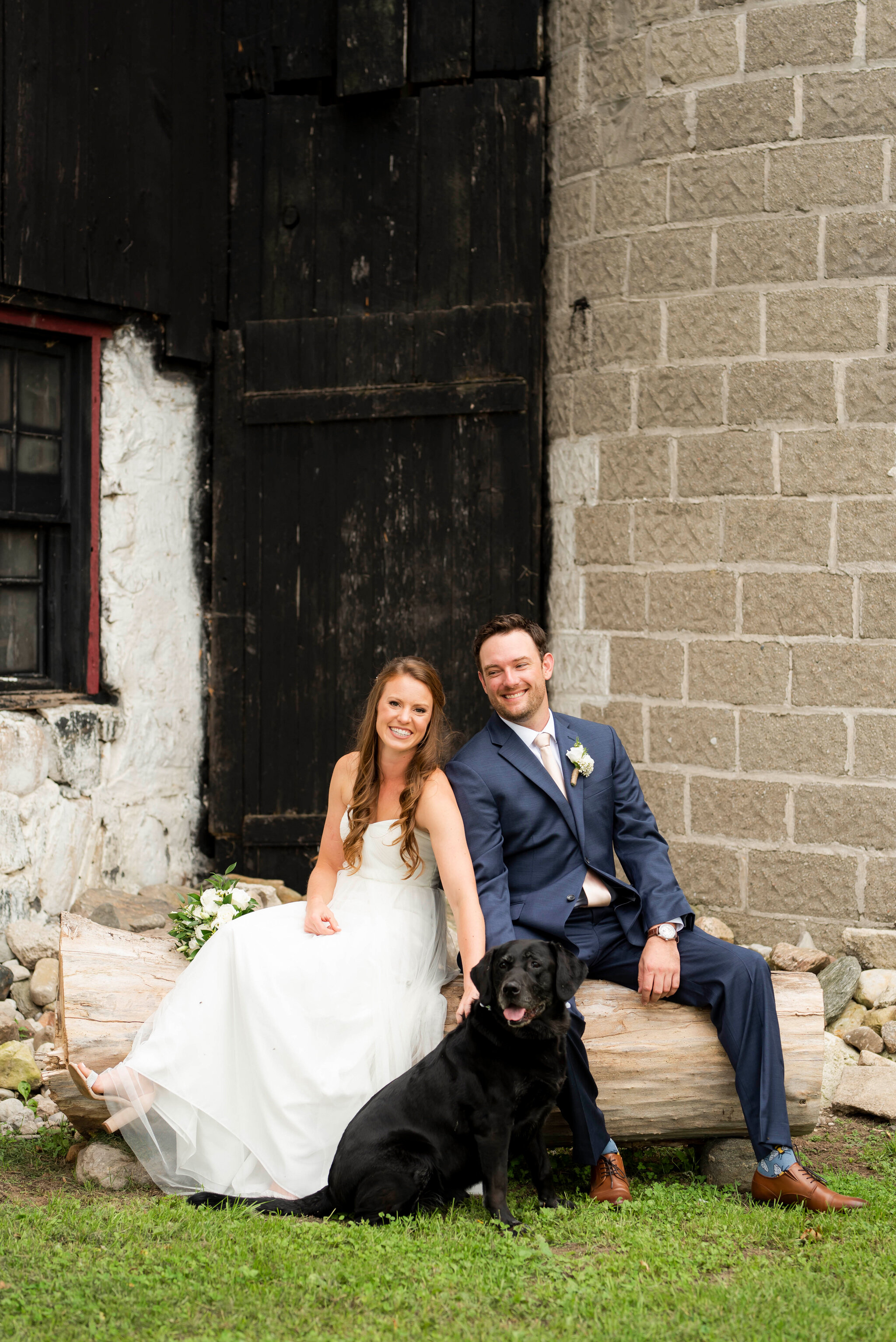 Bride and groom pose with dog outside barn