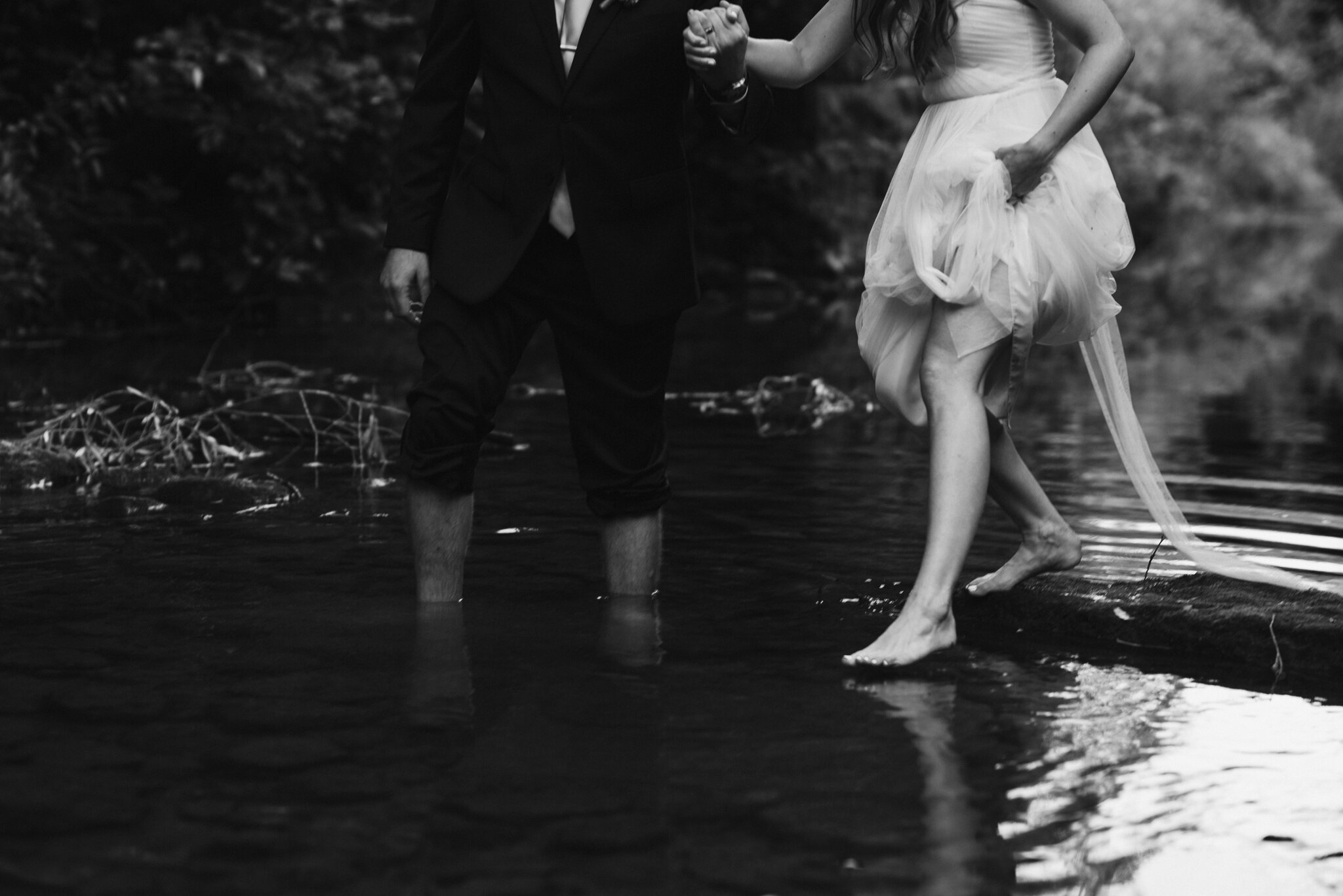 bride and groom wade in the river after getting married in backy