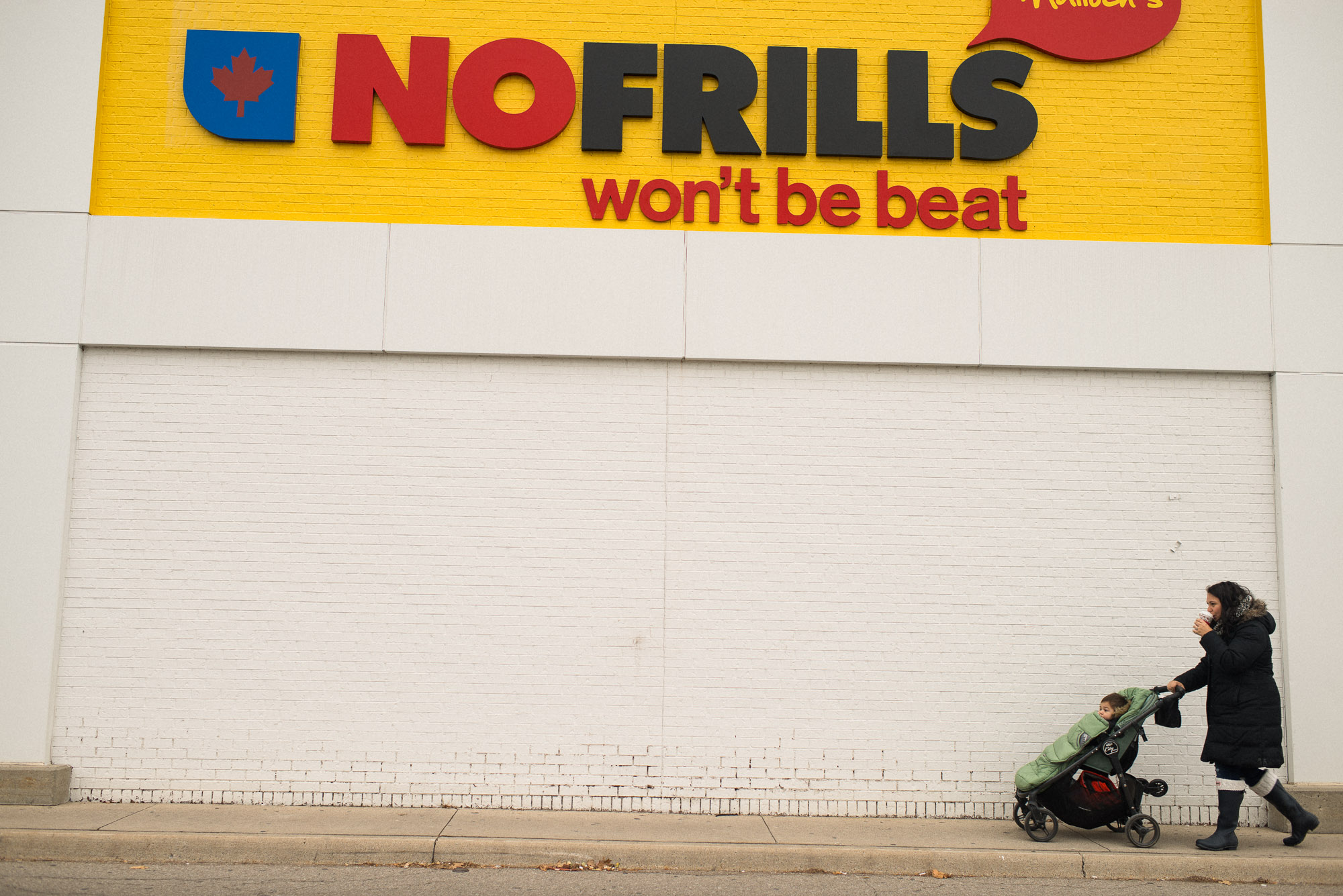 mom with coffee pushes stroller in front of no frills