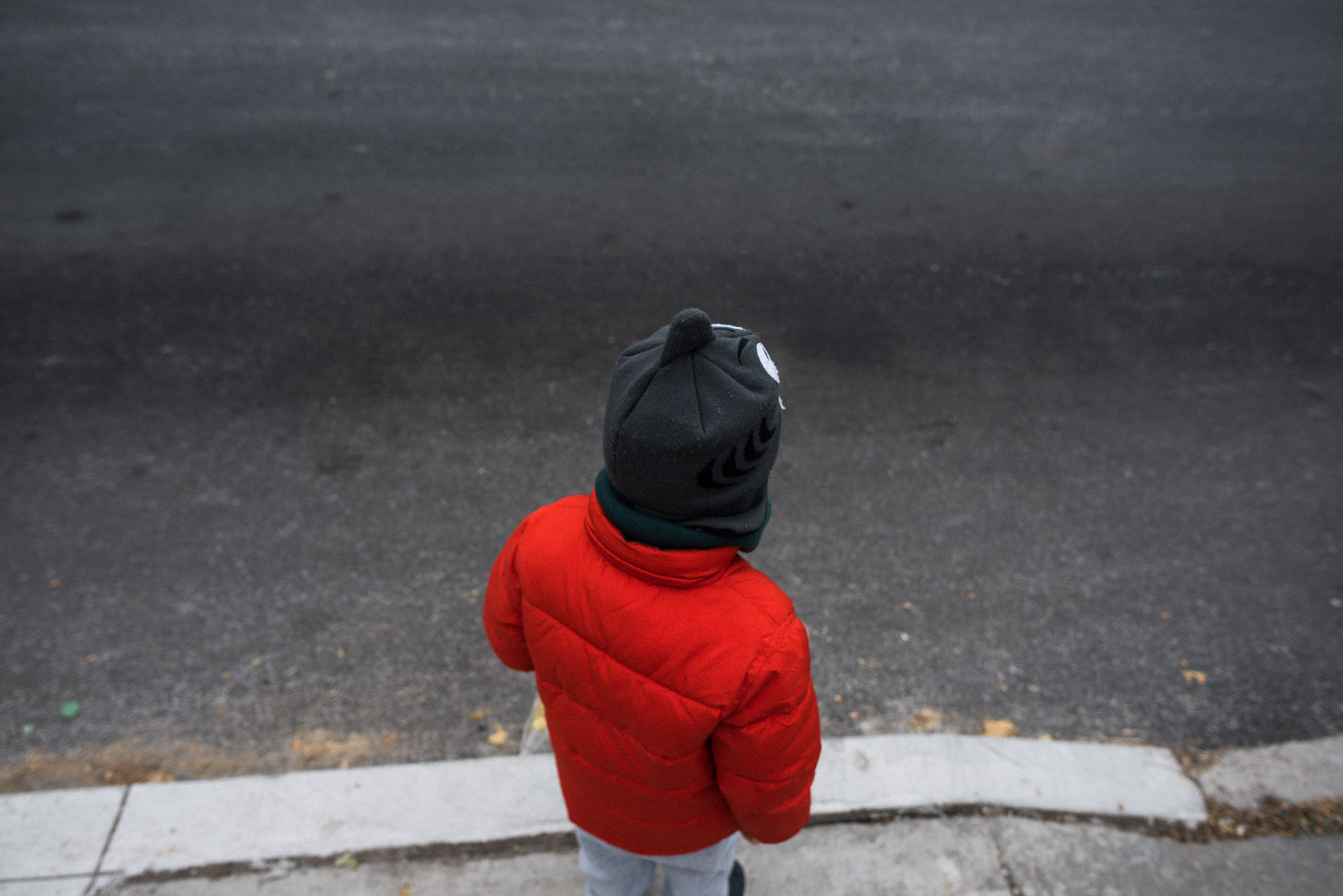 boy in orange coat stands at the curb