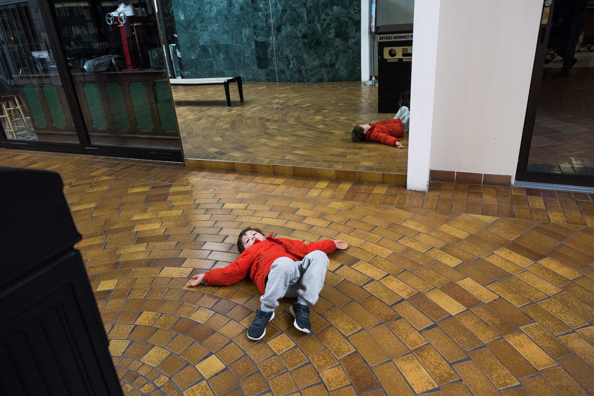 boy in orange coat lays on the floor of the mall