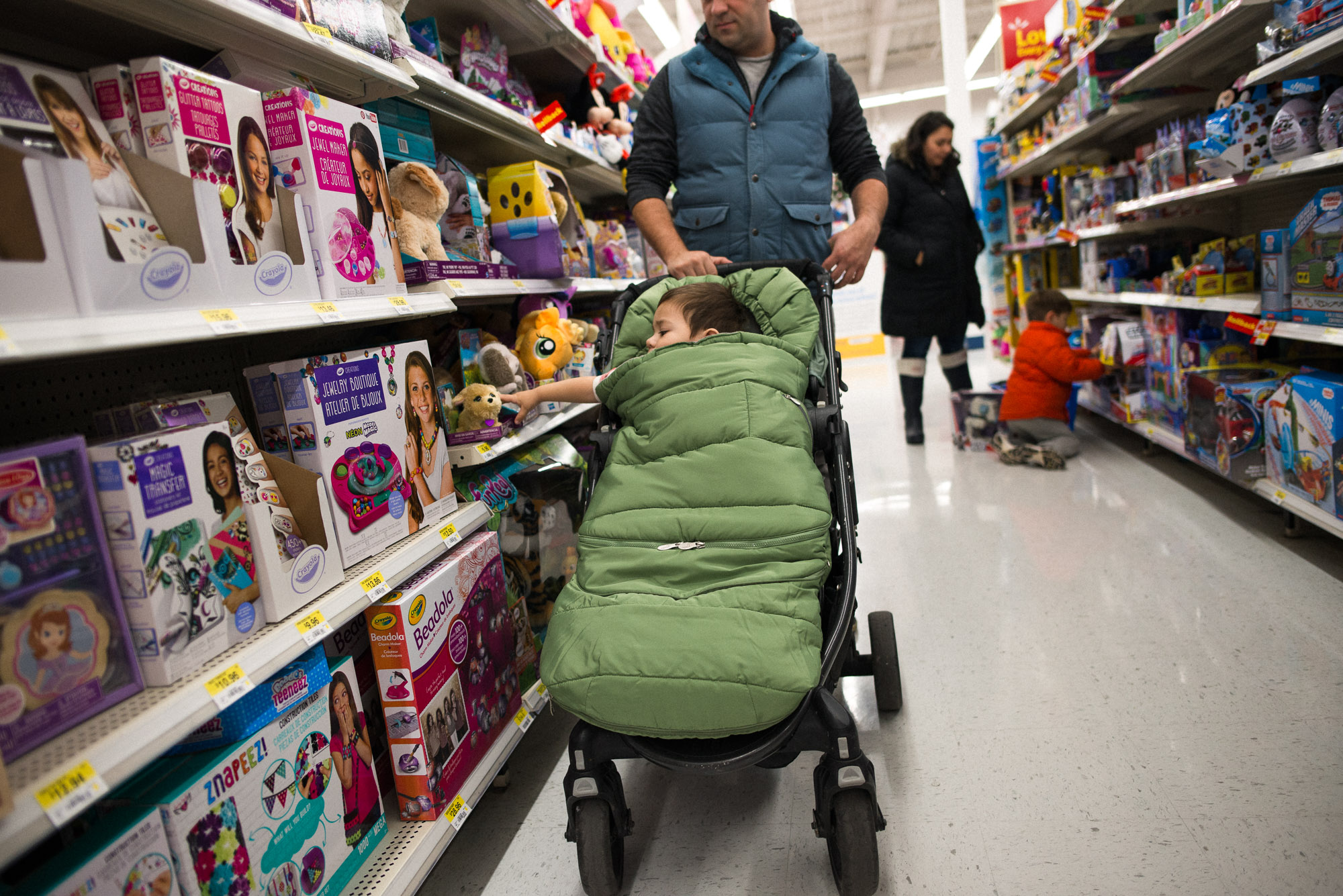 dad pushes stroller as toddler hand shoots out to grab toy off the shelf