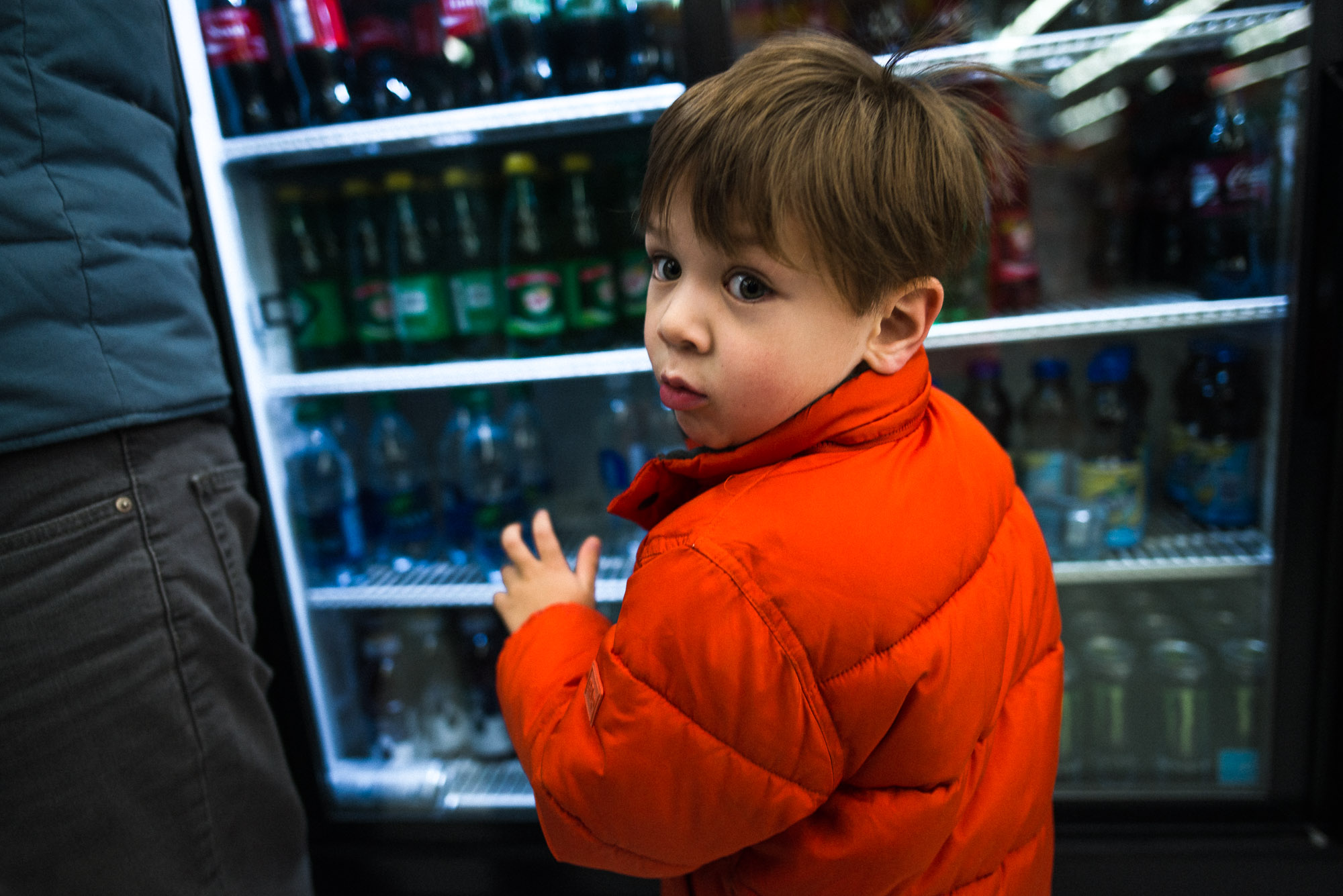 boy in orange coat looks back from a drink vending machine