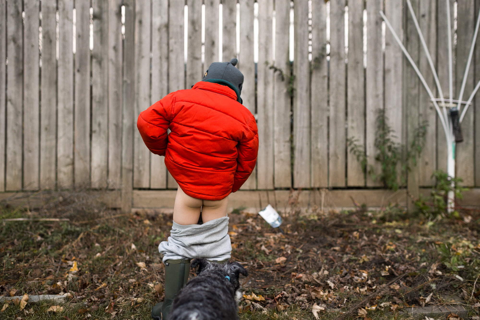 boy in orange coat pees outside